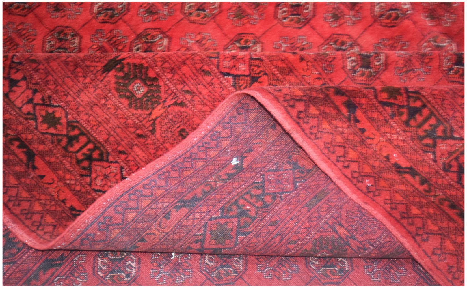 A vintage handmade Afghan Turkmen rug featuring a red field with repeating elephant foot motifs.
