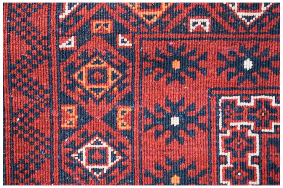 A vintage Afghan Turkmen rug featuring traditional geometric patterns in red, black, and orange.