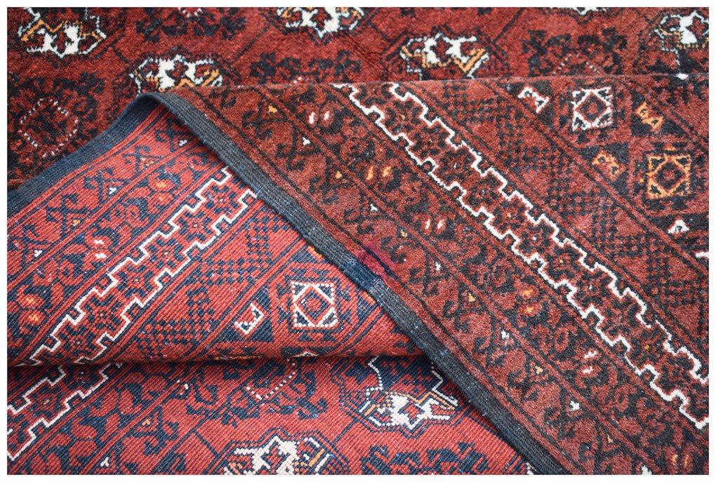 A vintage Afghan Turkmen rug featuring a red field with geometric elephant foot motifs.