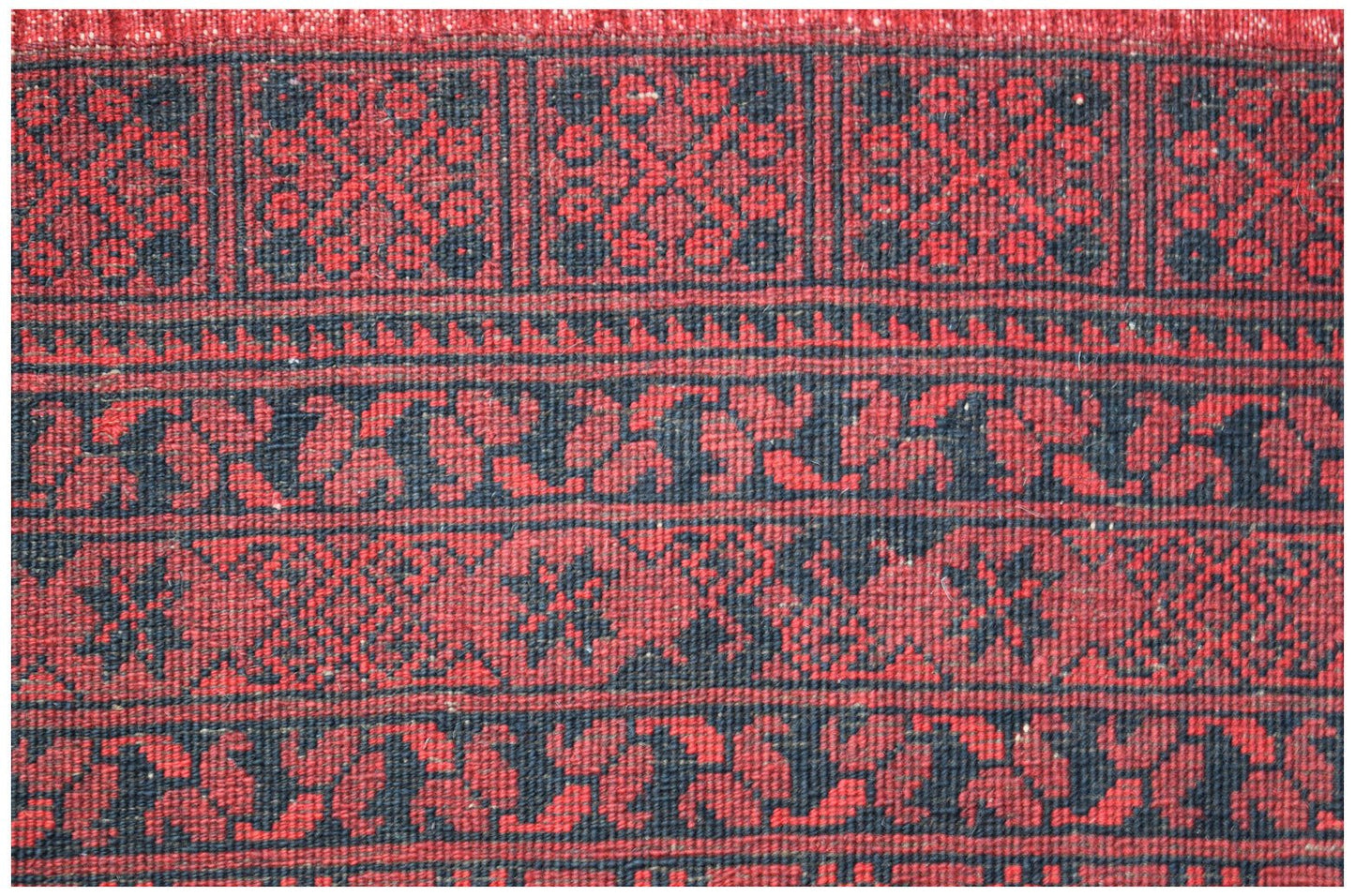 A vintage Afghan Turkmen rug featuring a repeating geometric elephant foot motif in red and black.