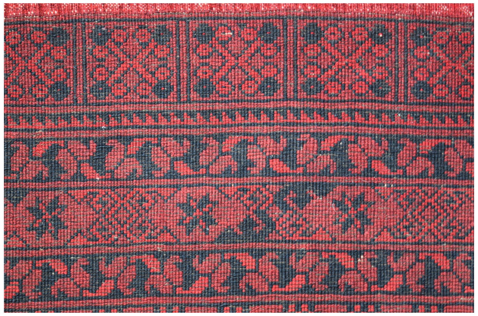 A vintage Afghan Turkmen rug featuring a repeating geometric elephant foot motif in red and black.
