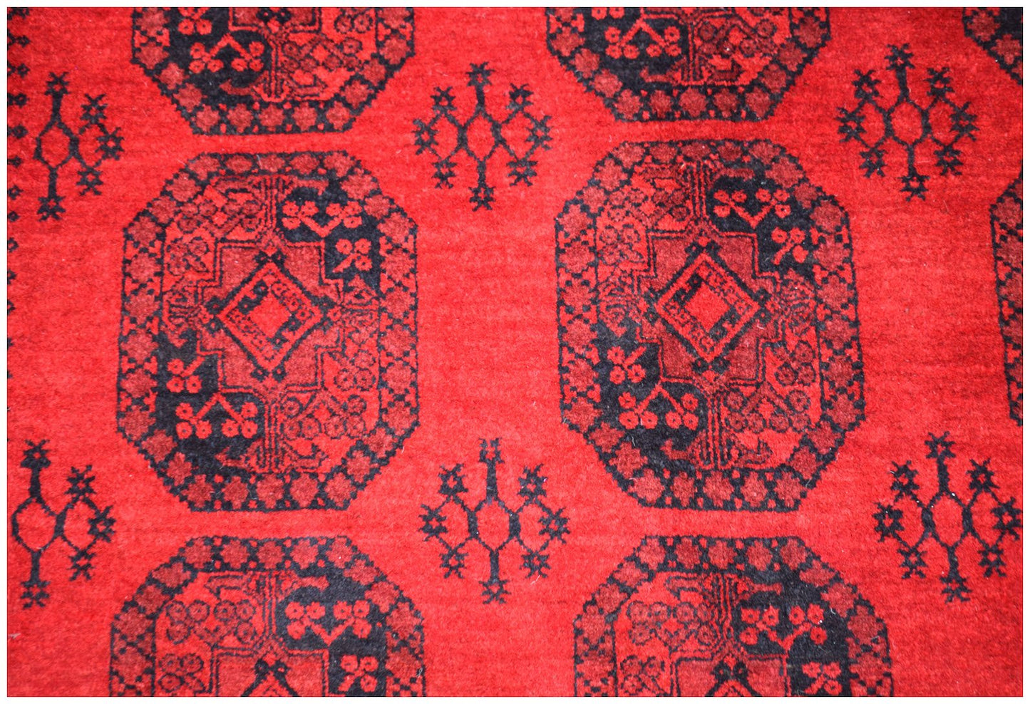 A vintage Afghan Turkmen rug featuring a repeating black elephant foot motif on a red wool field.