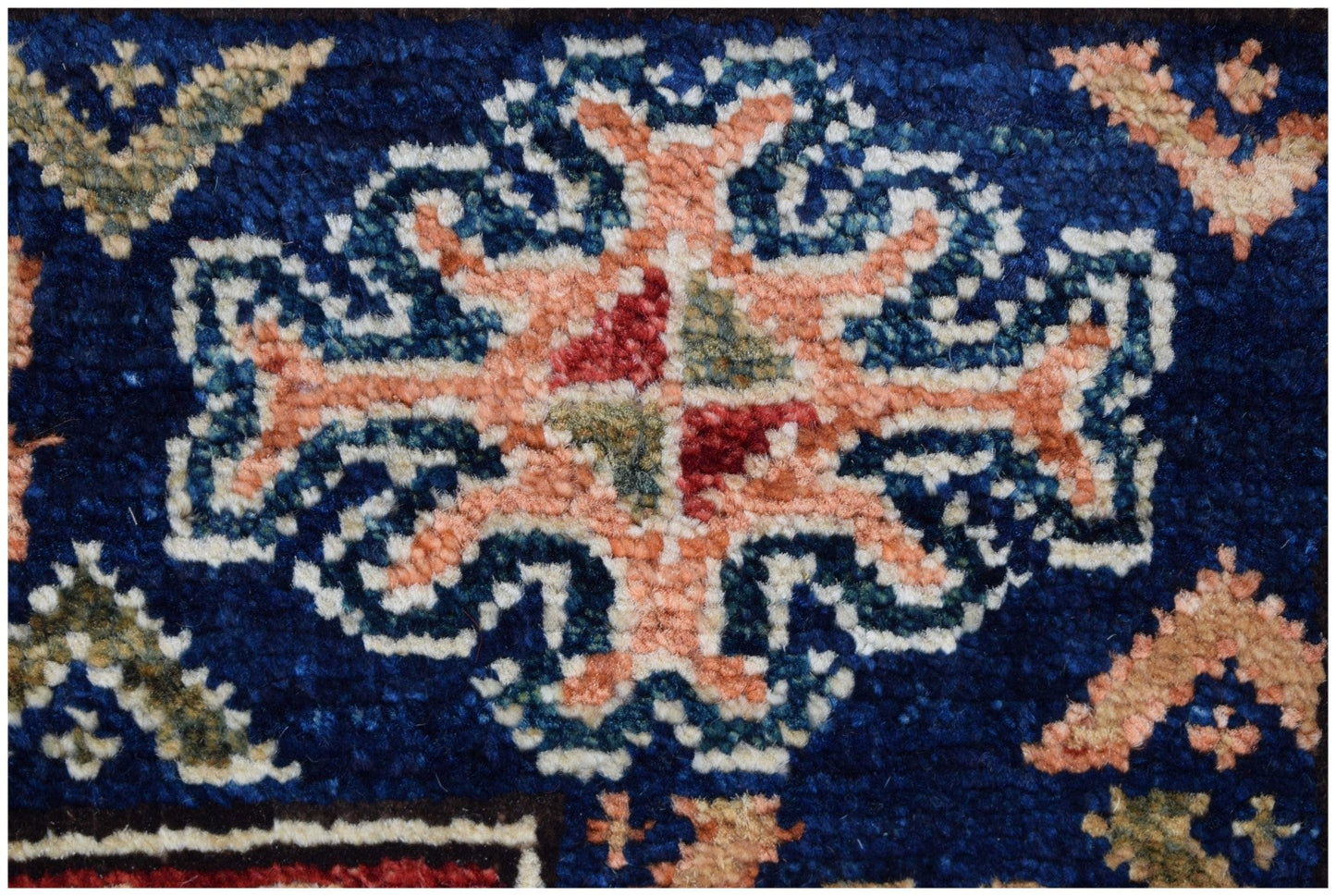 A close-up of an Afghan Chobi runner featuring a central floral motif in peach, blue, and red.