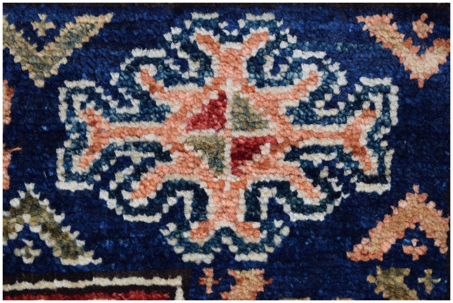 A close-up of an Afghan Chobi runner featuring a central floral motif in peach, blue, and red.
