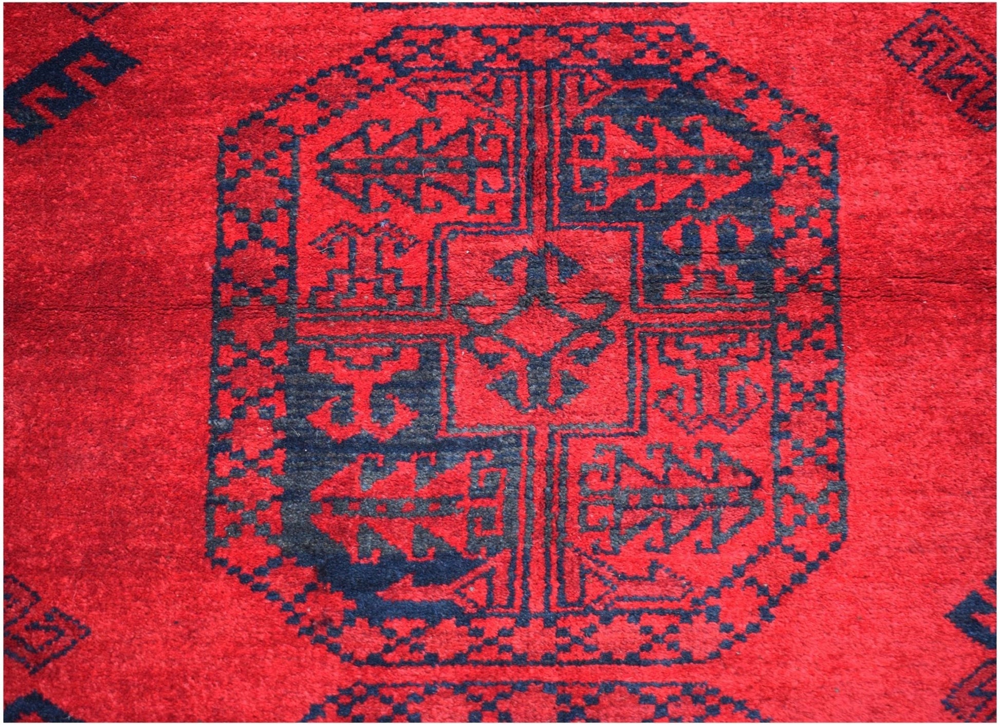 A vintage Afghan Turkmen rug featuring a traditional dark blue elephant foot motif on a red field.