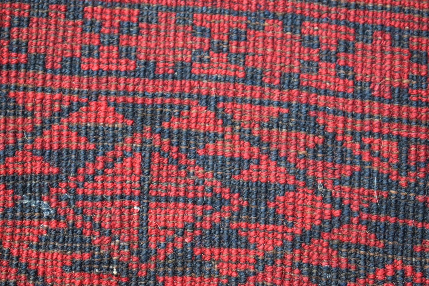 A close-up of a vintage Afghan Turkmen rug featuring a geometric red and black pattern.
