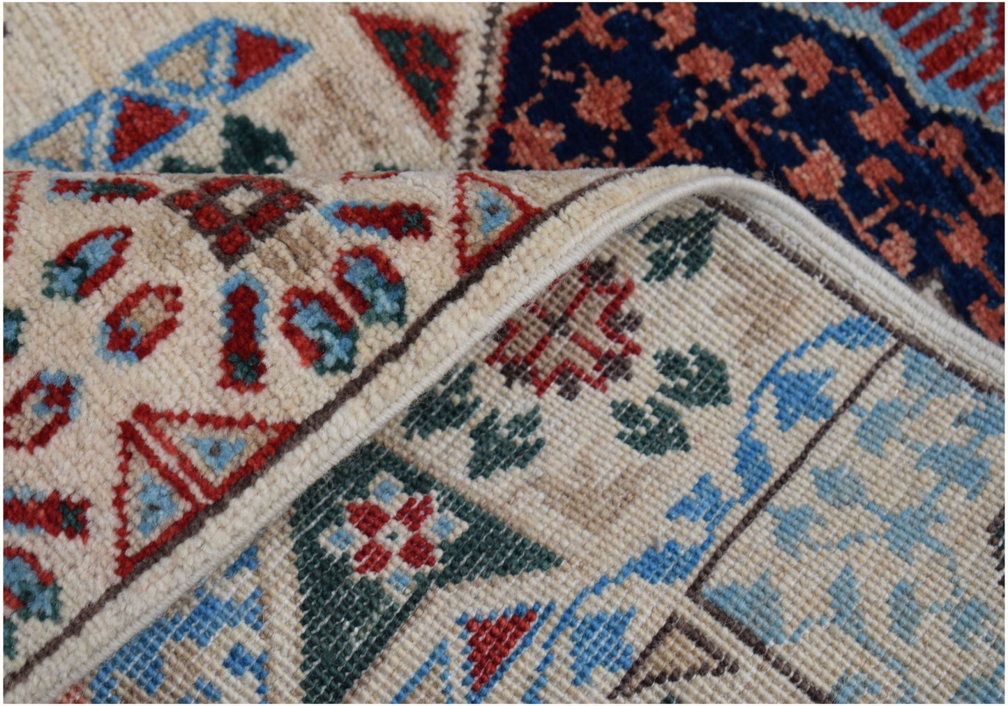 A close-up of a handmade Afghan Chobi runner featuring intricate geometric patterns in red, blue, and green on a cream wool base.
