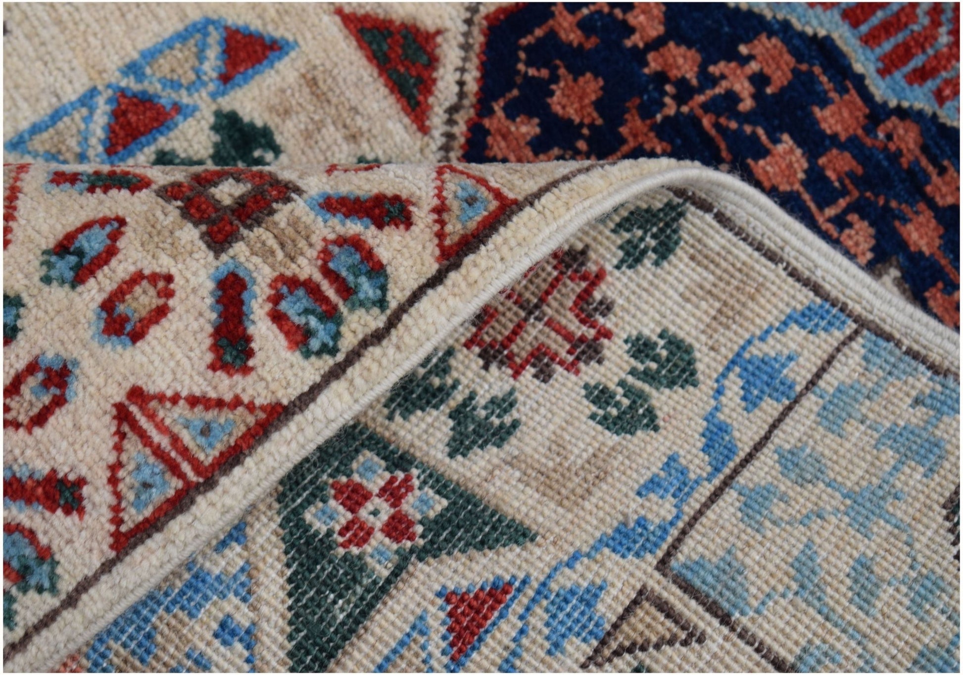A close-up of a handmade Afghan Chobi runner featuring intricate geometric patterns in red, blue, and green on a cream wool base.