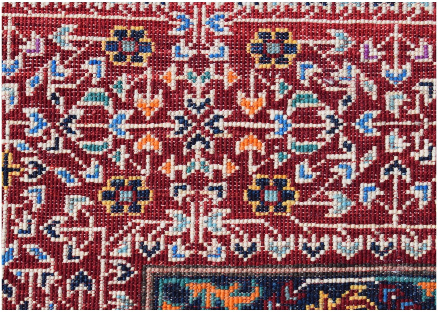 A close-up of a handmade Afghan Chobi rug featuring intricate geometric floral patterns in red.