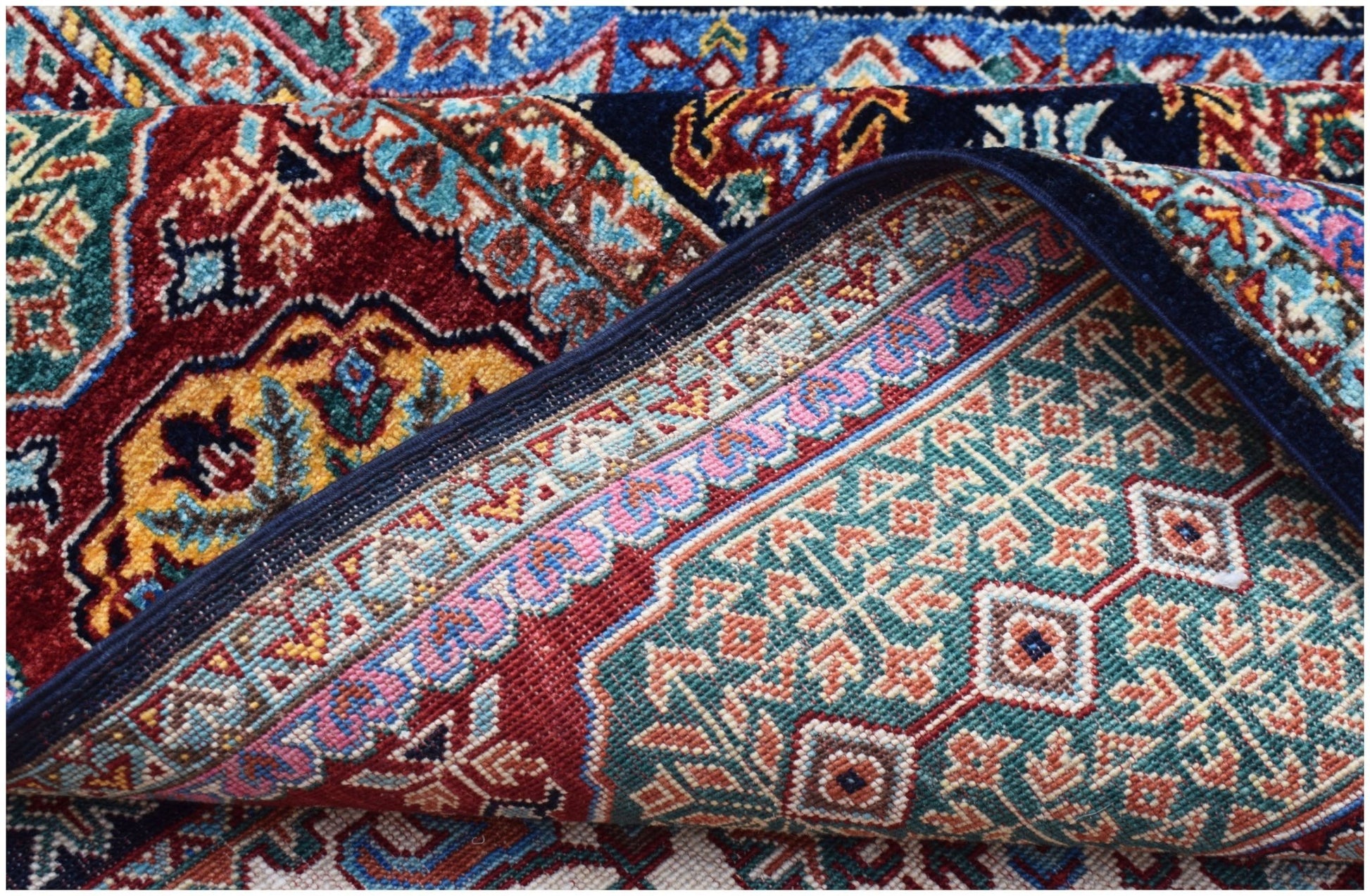 A corner of a handwoven Afghan Chobi rug with a Mamluk pattern in red, blue, and teal tones.