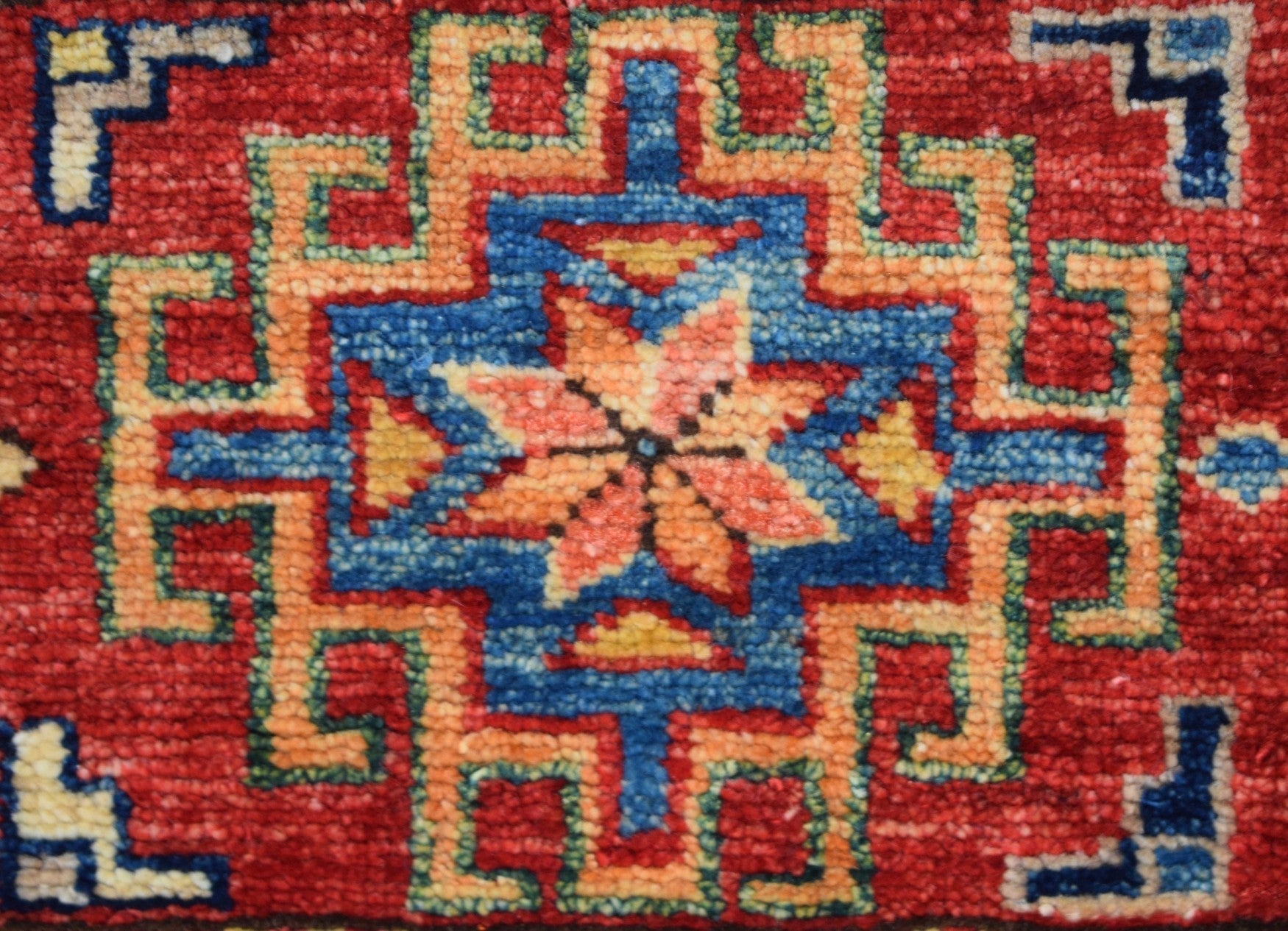 A handmade Afghan Super Kazakh rug featuring a geometric star motif in red, blue, and orange.