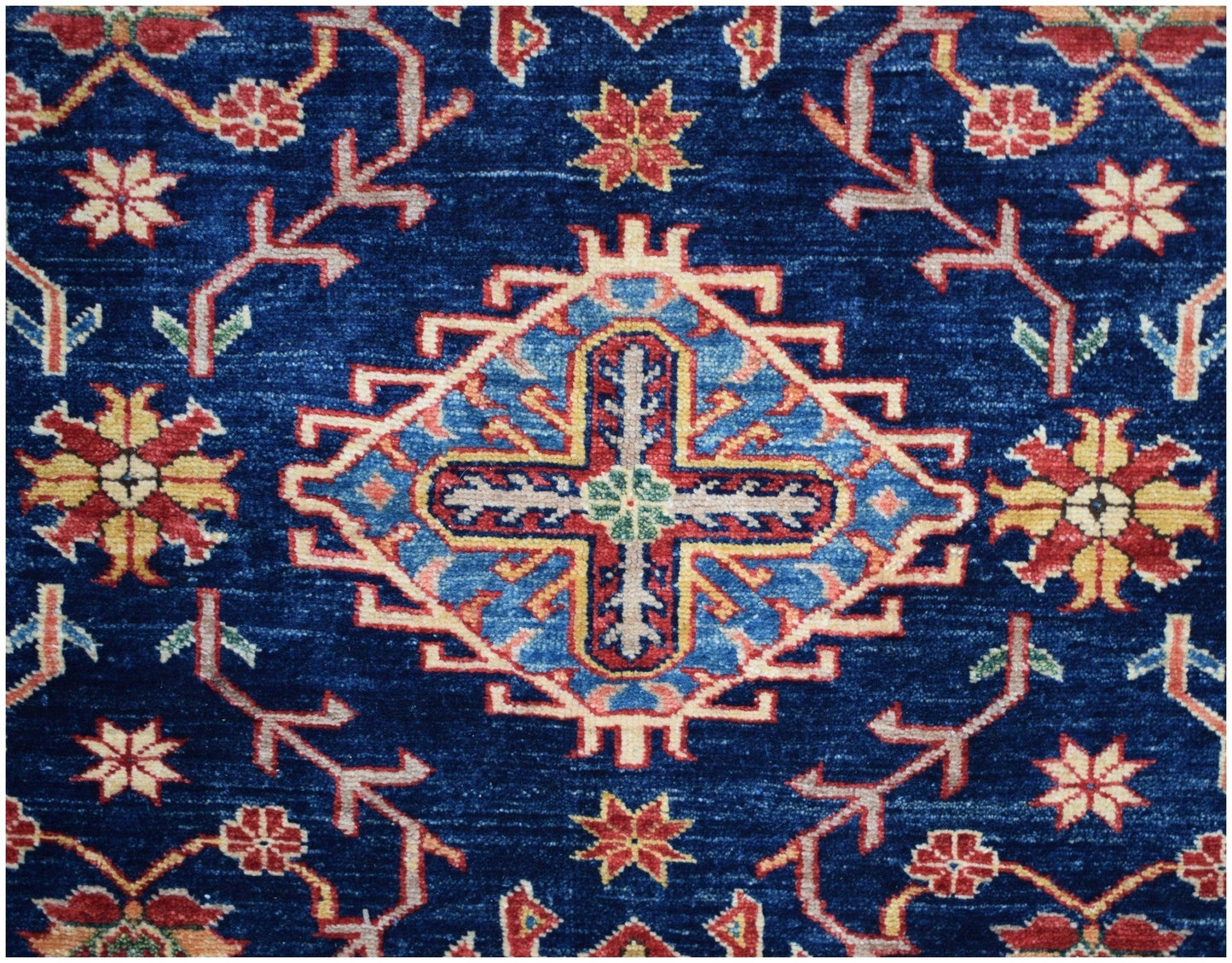 Handmade Afghan Kazakh rug featuring a central geometric cross motif on a deep blue field.