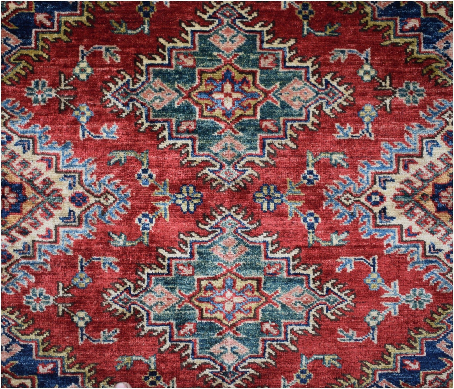 Handmade Afghan Super Kazakh rug featuring a geometric medallion pattern in red, blue, and green.