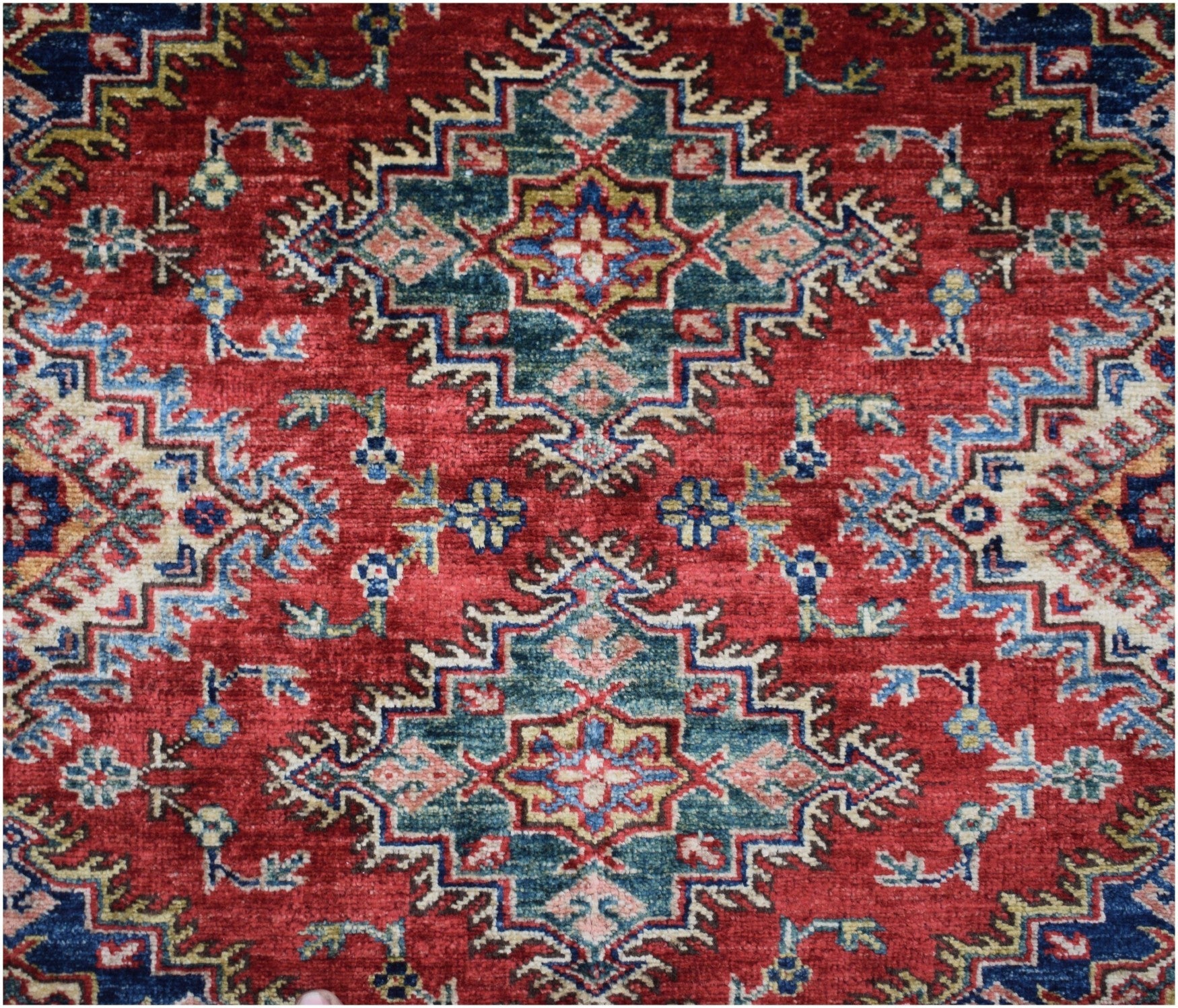 Handmade Afghan Super Kazakh rug featuring a geometric medallion pattern in red, blue, and green.