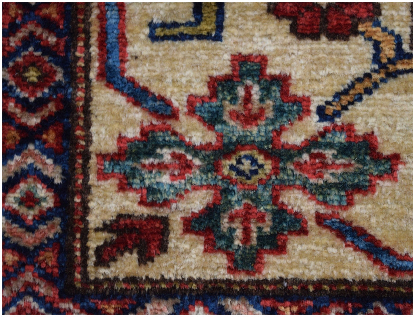 A close-up of an Afghan Super Kazakh rug featuring a geometric floral motif in red, blue, and green.