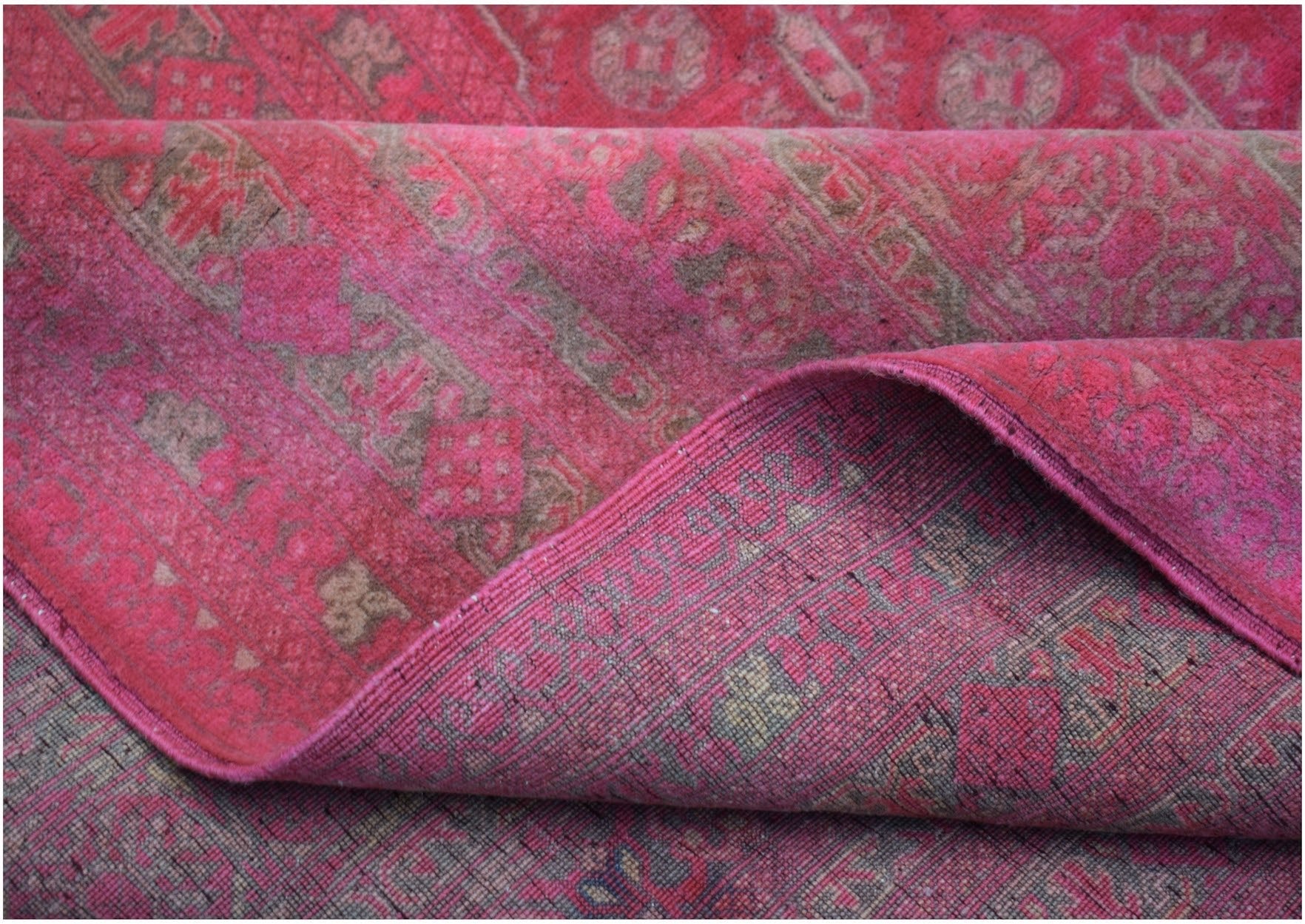 A folded vintage Afghan Turkmen rug featuring a geometric pattern in shades of pink and brown.
