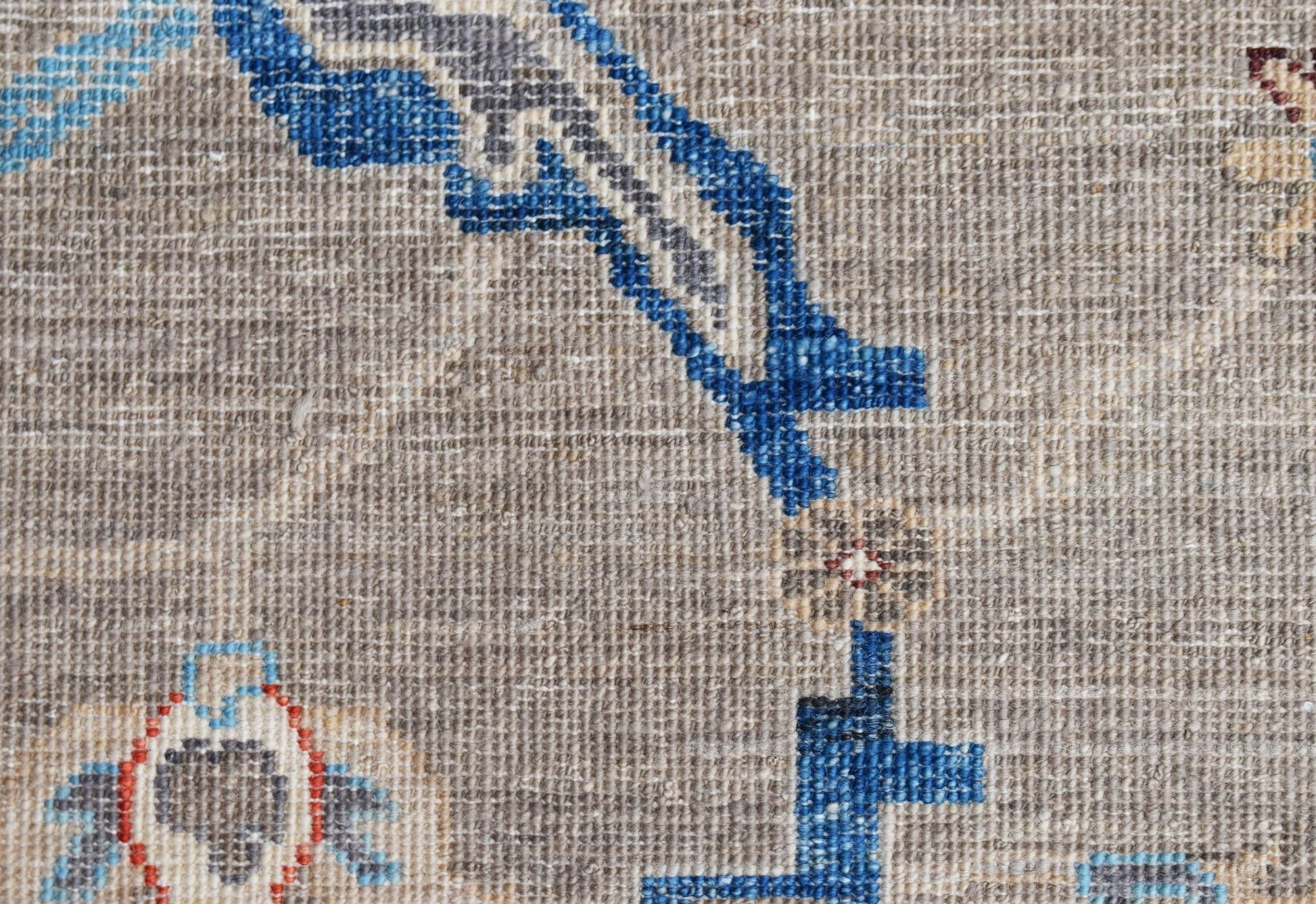 A close-up of a handwoven Afghan Chobi rug featuring intricate blue floral patterns on a beige wool base.