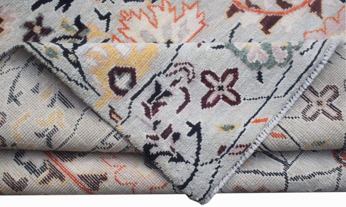 A hand-knotted wool rug featuring a transitional floral pattern in orange, yellow, and dark brown.