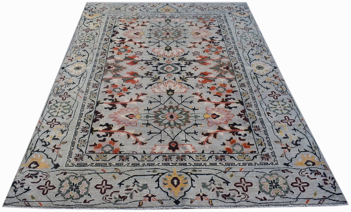 A hand-knotted wool rug featuring a light blue background with floral and geometric patterns.