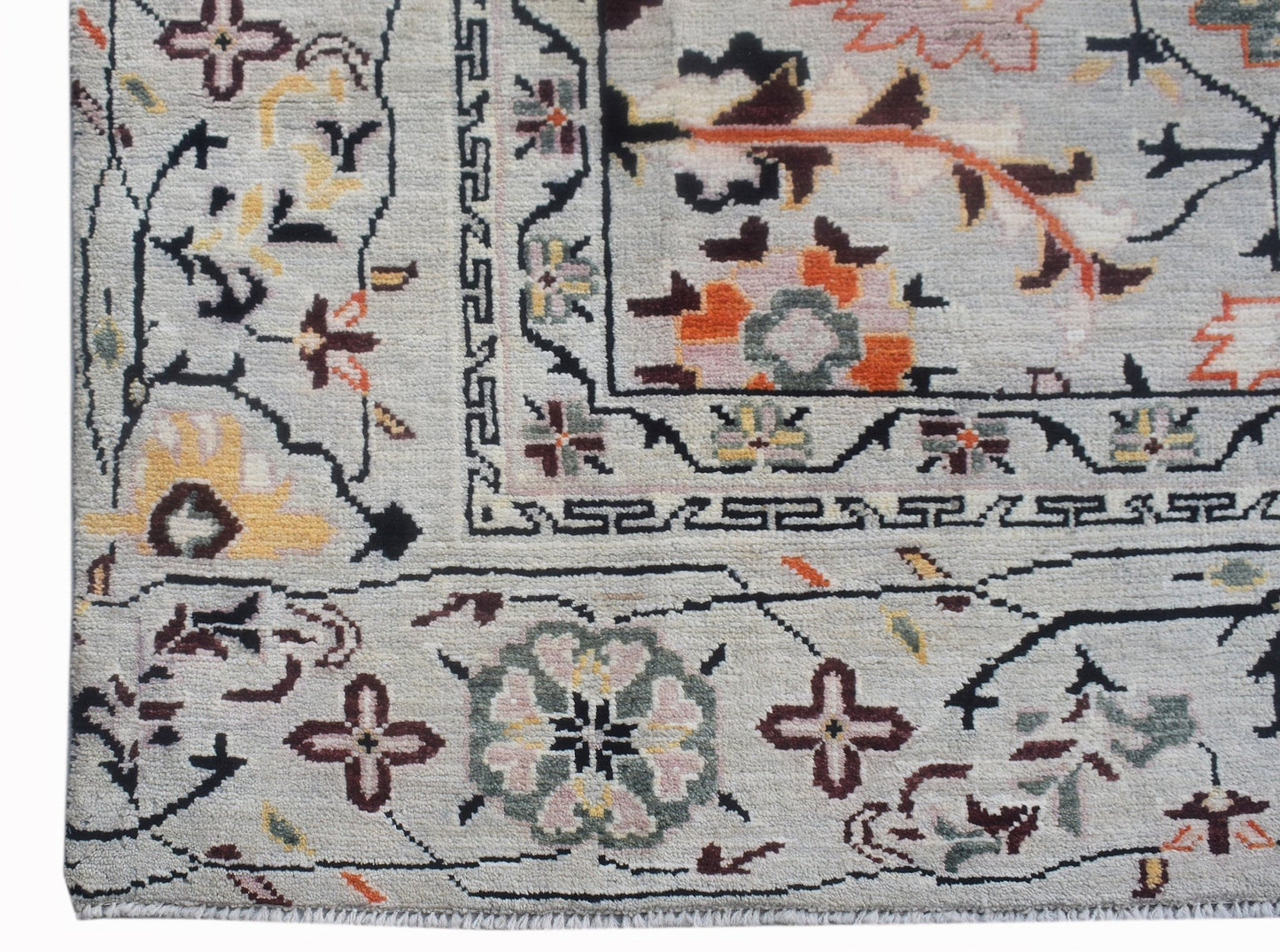 A hand-knotted wool rug featuring a light grey background with intricate floral and geometric motifs.