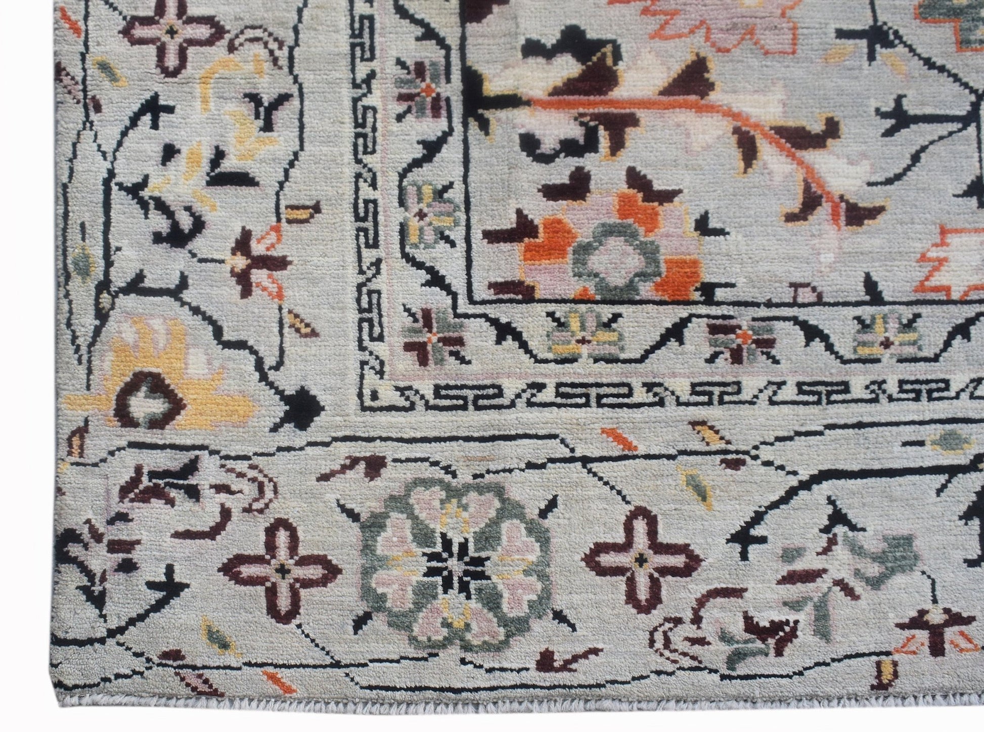 A hand-knotted wool rug featuring a light grey background with intricate floral and geometric motifs.