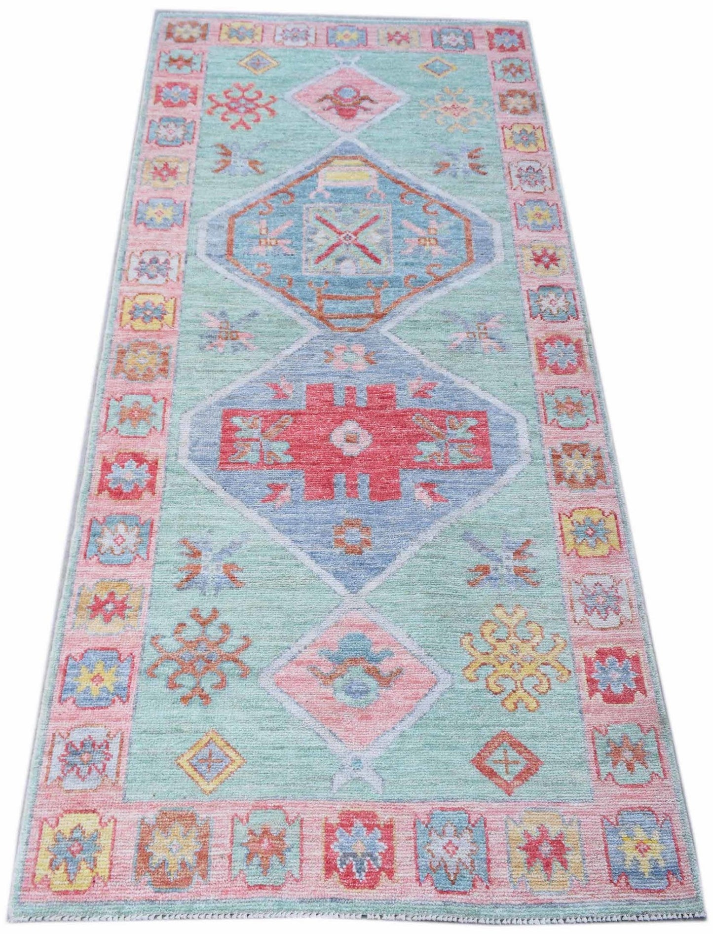 A handwoven wool runner rug featuring a light blue field with geometric diamond motifs.