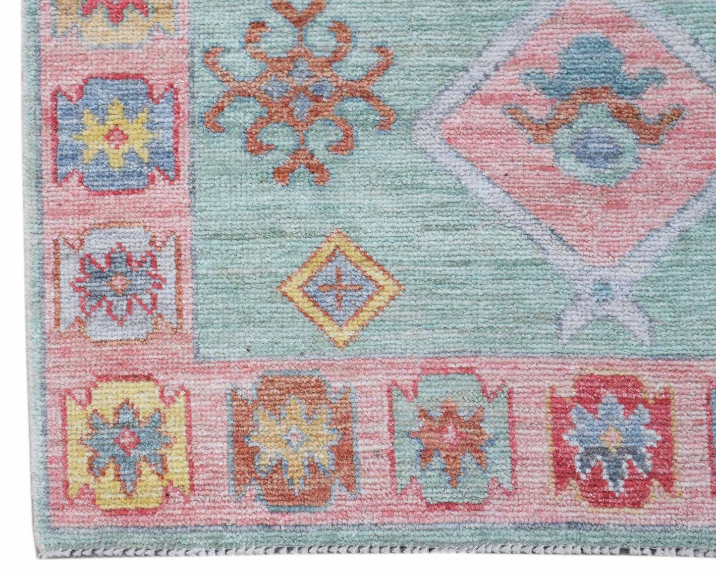 A handwoven wool runner featuring a light blue field with pink borders and geometric floral motifs.