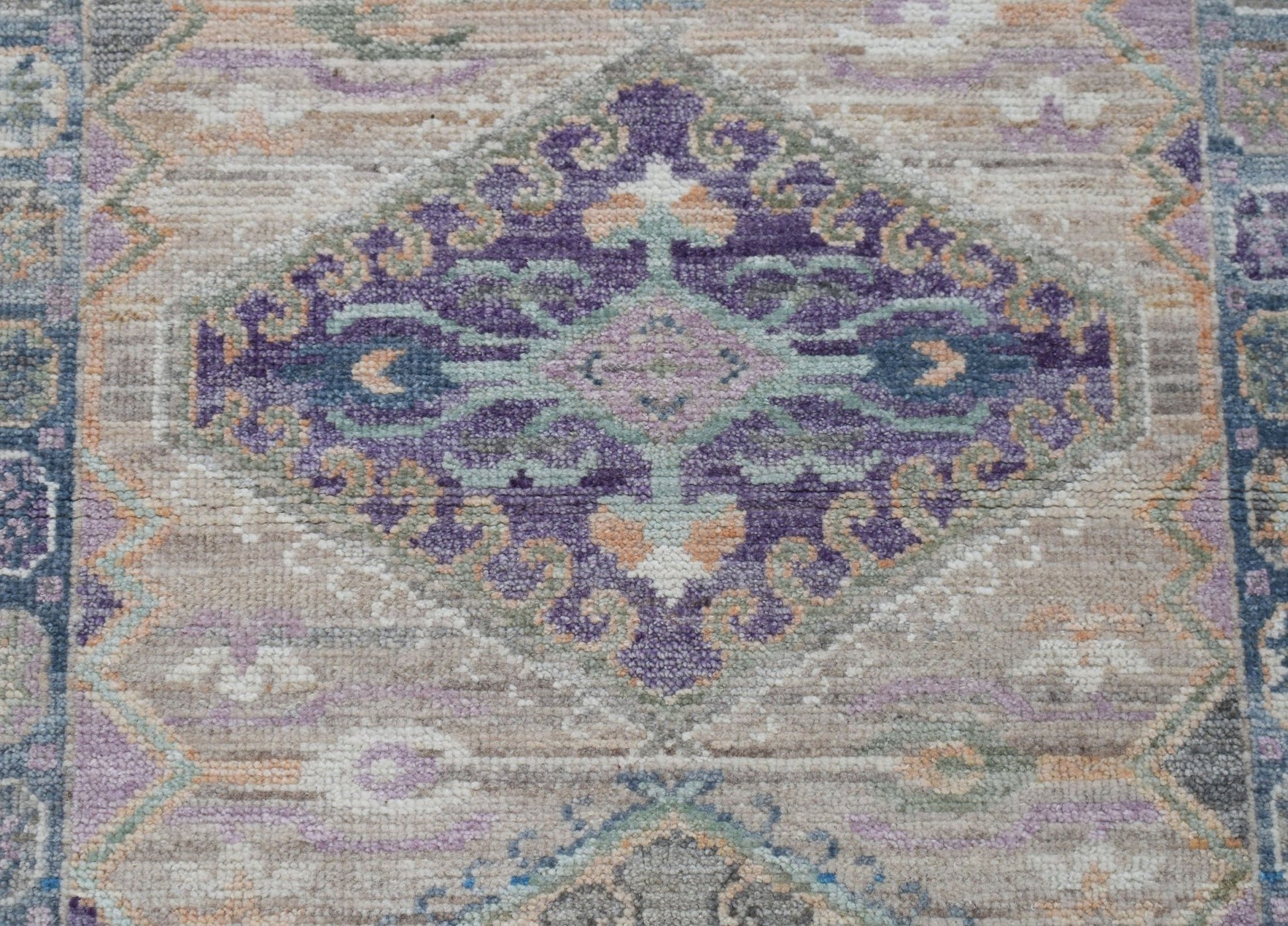A handwoven wool runner rug featuring a central purple diamond medallion on a neutral background.