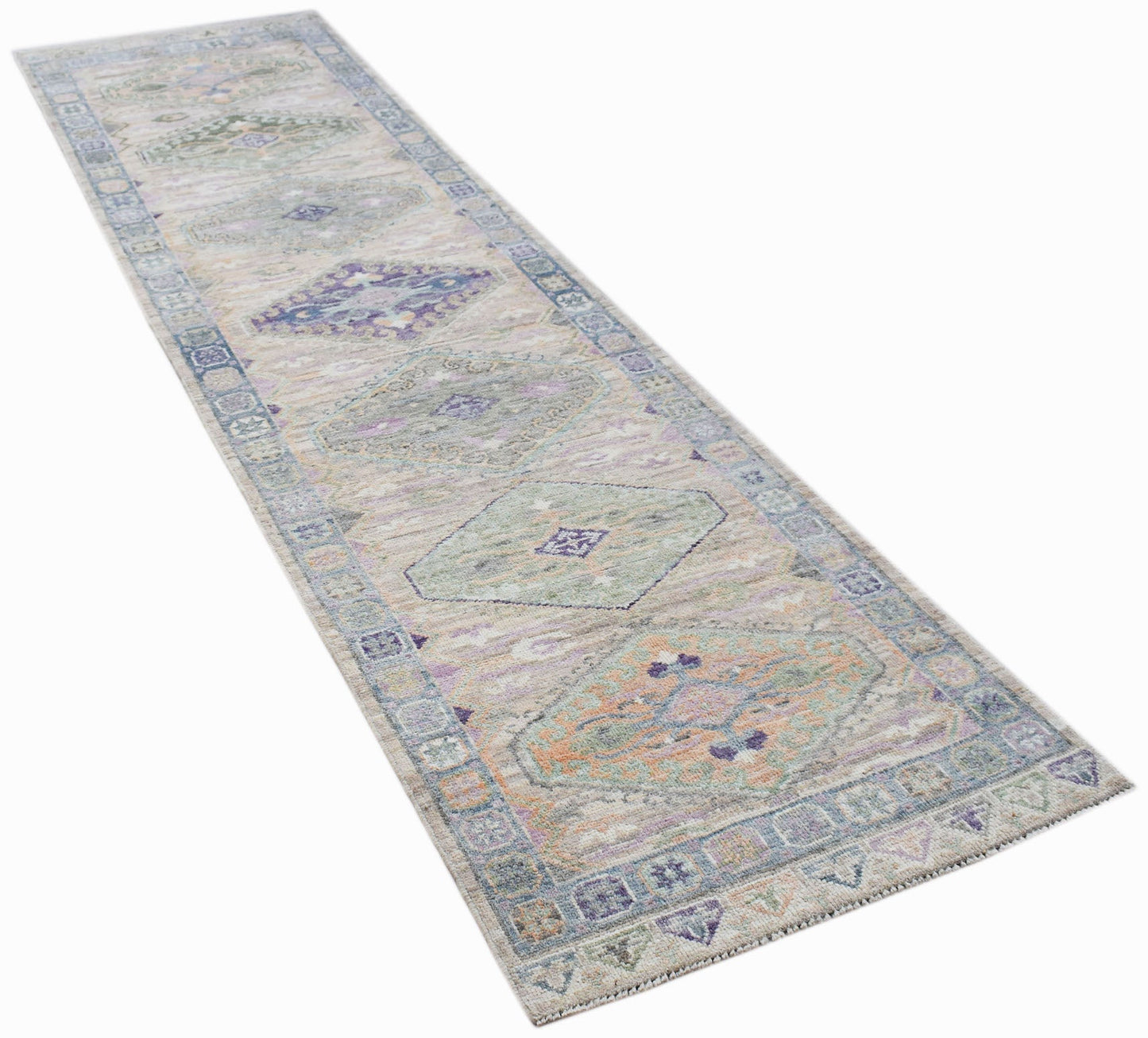 A handwoven wool runner rug featuring a transitional Oushak pattern in muted pastel tones.