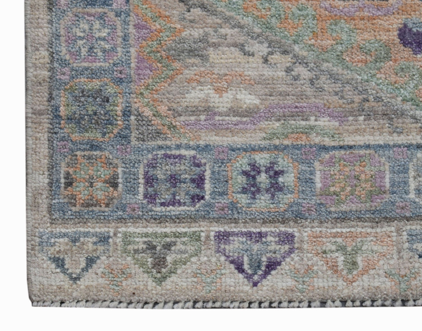 A close-up of a handwoven Oushak runner featuring a geometric border in blue, purple, and green.