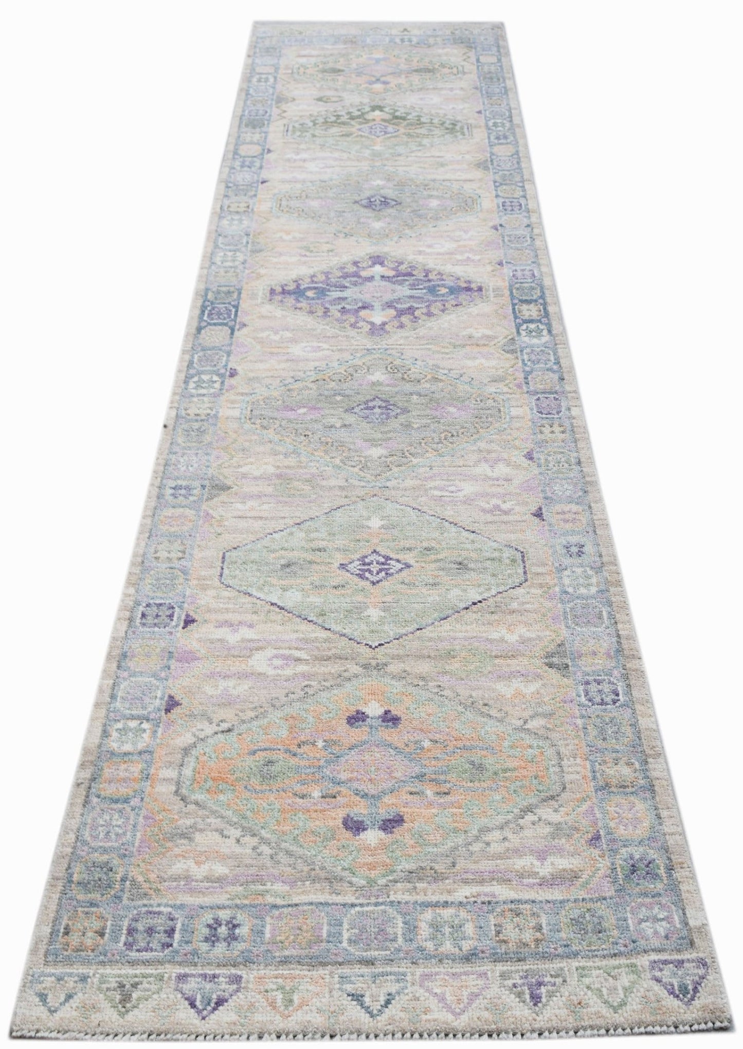 A handwoven wool runner rug featuring a transitional Oushak pattern in soft pastel tones.