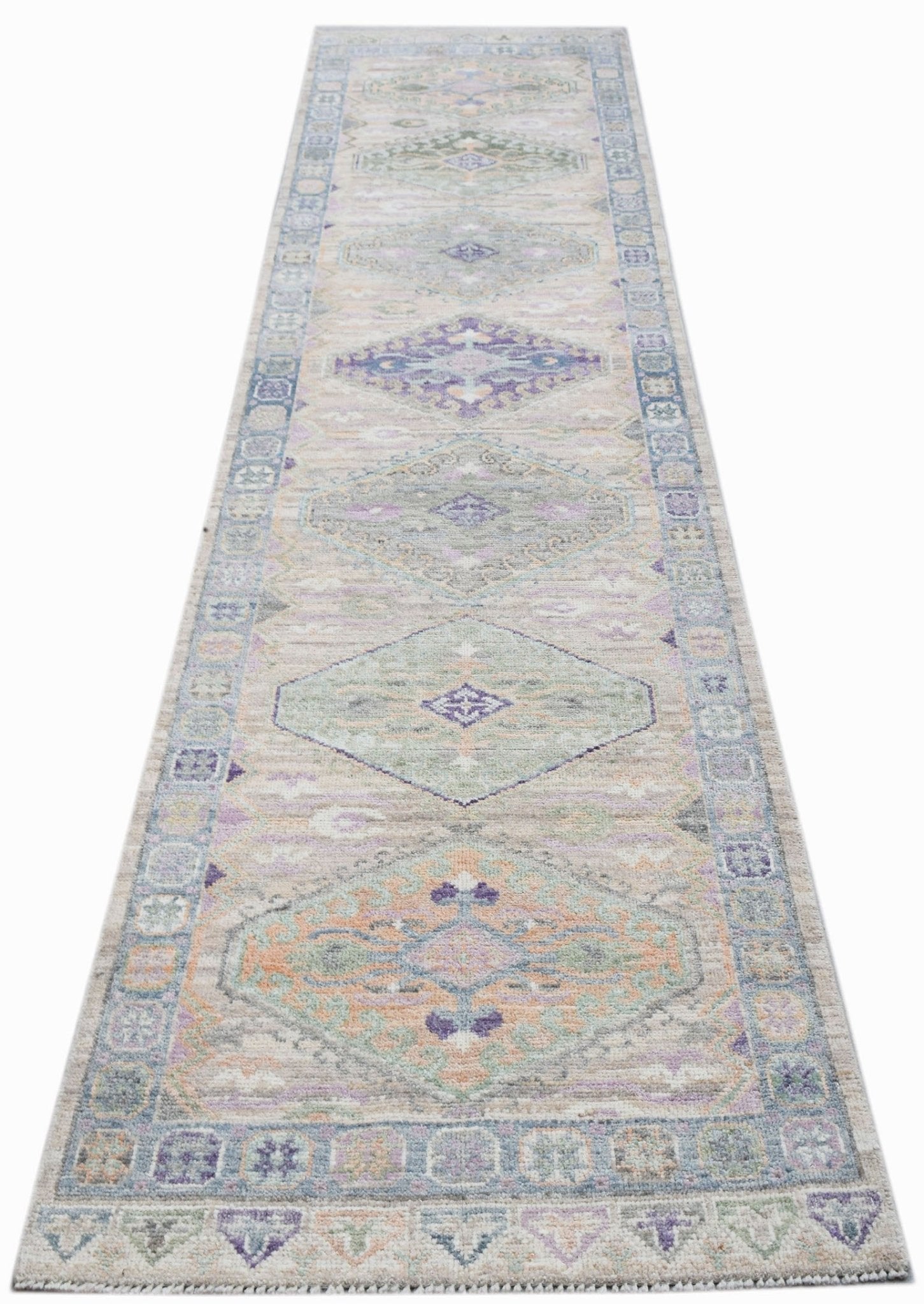 A handwoven wool runner rug featuring a transitional Oushak pattern in soft pastel tones.