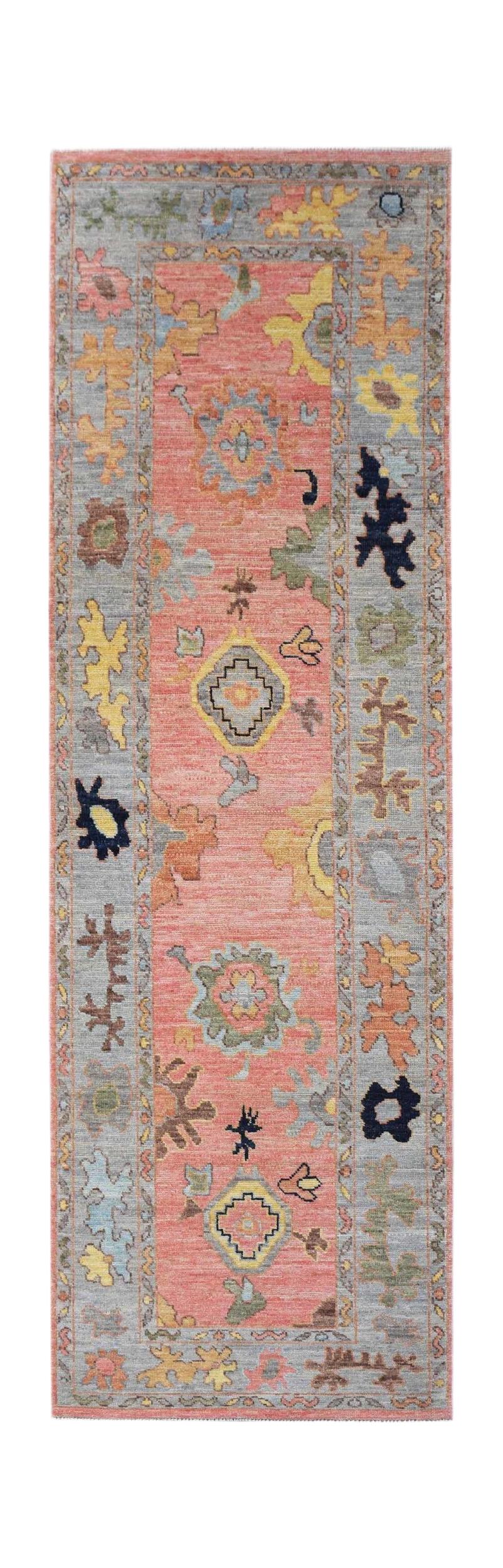 A handwoven wool runner rug featuring a coral center with floral motifs and a grey border.