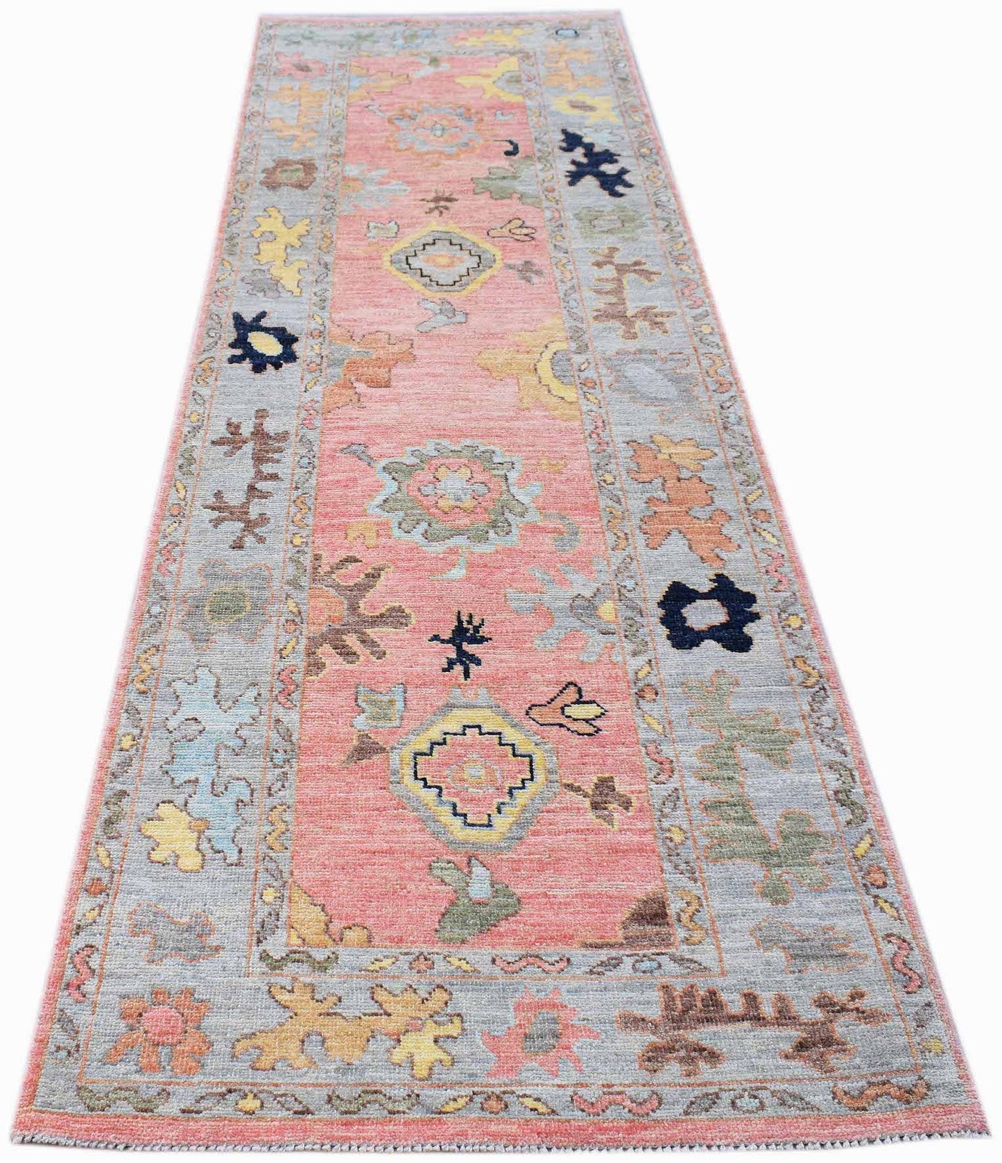 A handwoven transitional Oushak runner featuring a floral pattern in pink, grey, and muted tones.