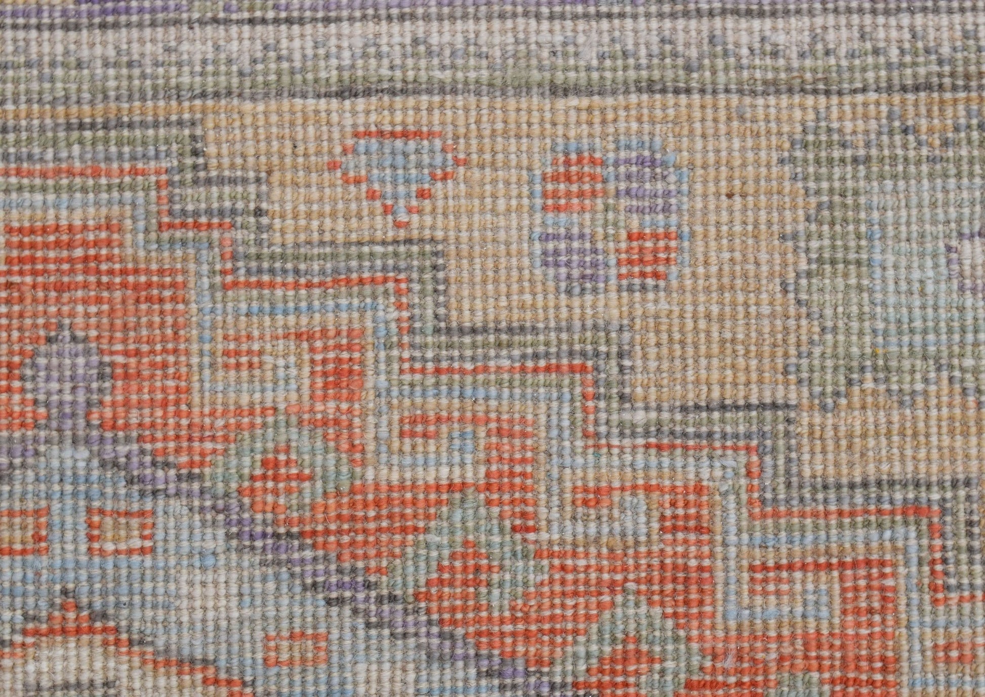 A close-up of a handwoven transitional Oushak rug featuring geometric patterns in orange and blue.