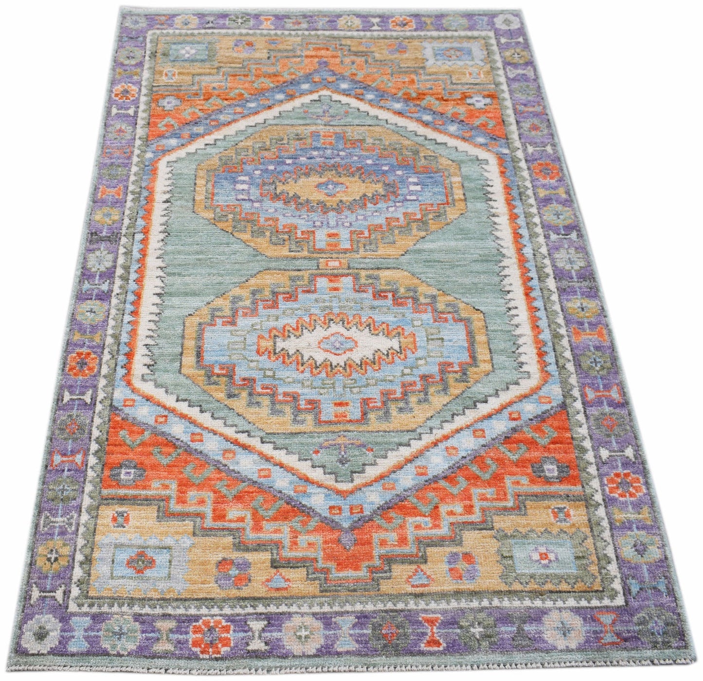 A handwoven transitional Oushak rug featuring geometric patterns in blue, orange, and purple.