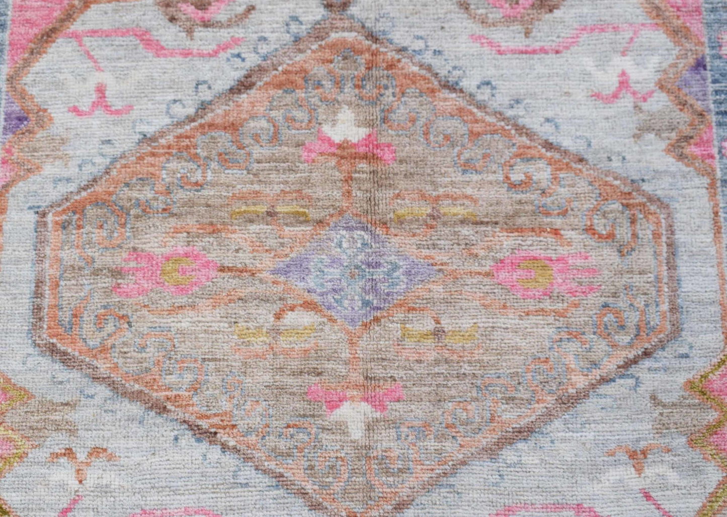 A transitional Oushak rug featuring a central floral medallion in soft pink, blue, and tan tones.