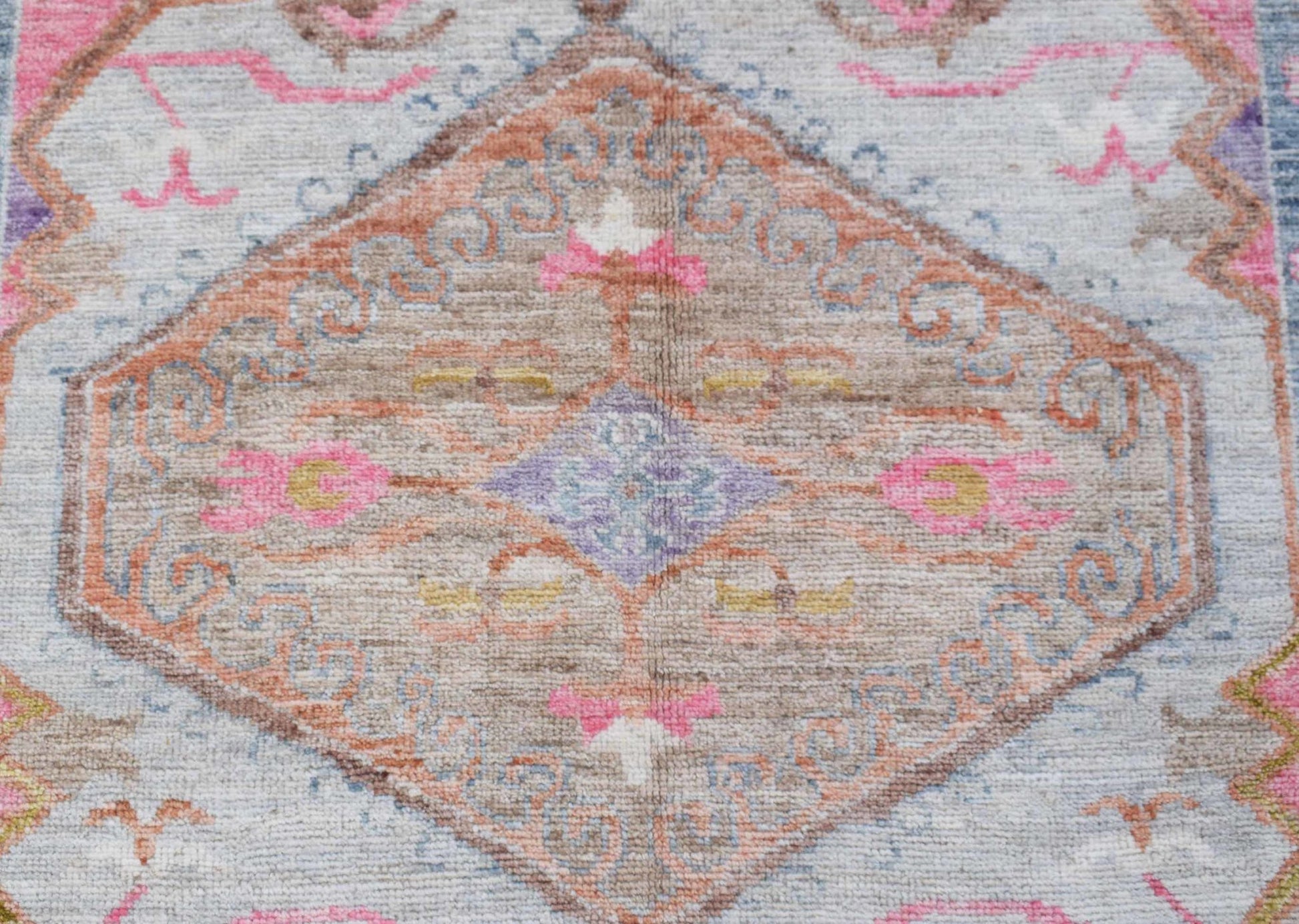 A transitional Oushak rug featuring a central floral medallion in soft pink, blue, and tan tones.