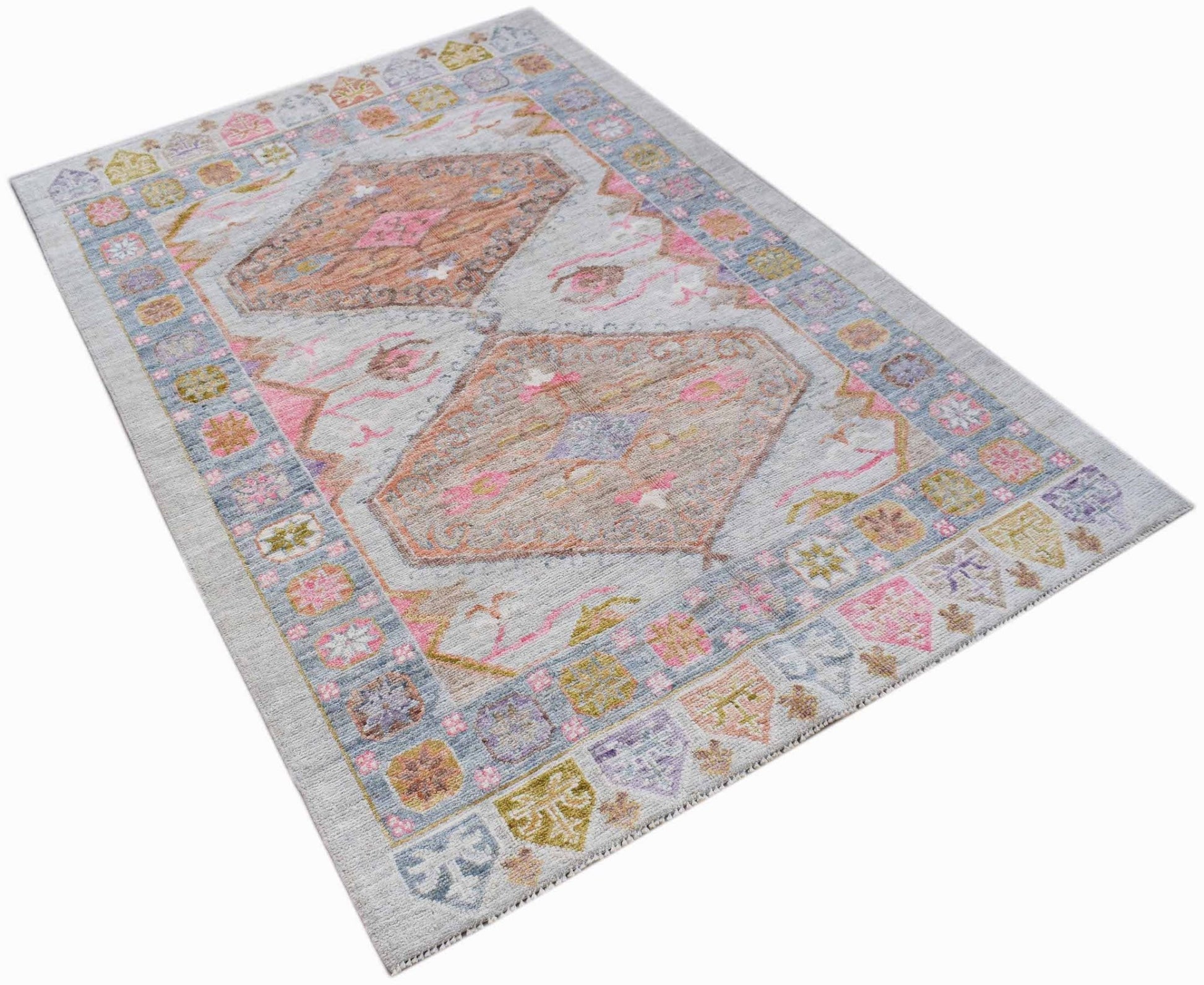A handwoven transitional Oushak rug featuring a light grey field with pink and tan geometric motifs.