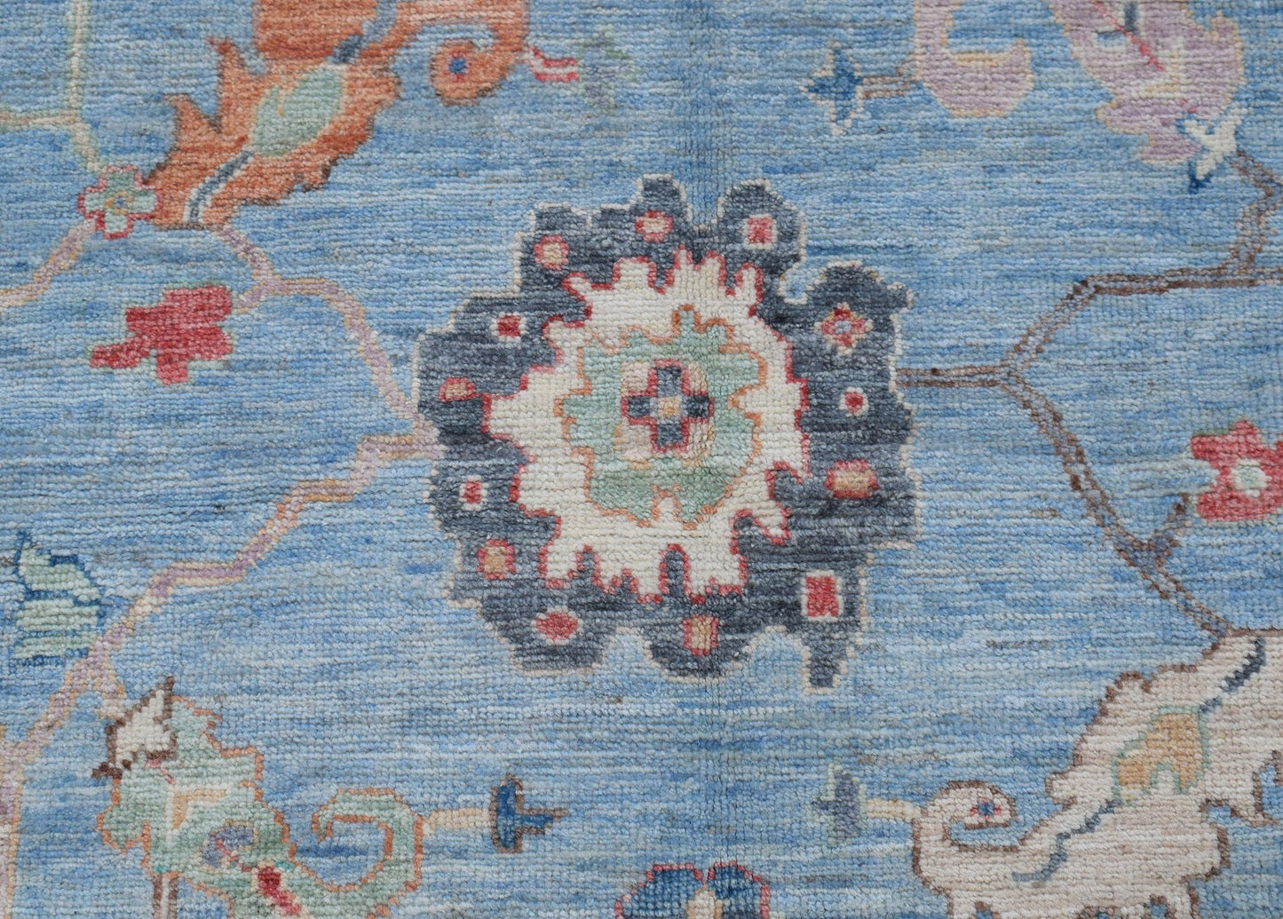 A handwoven transitional Oushak rug featuring a floral pattern in blue, cream, and muted tones.