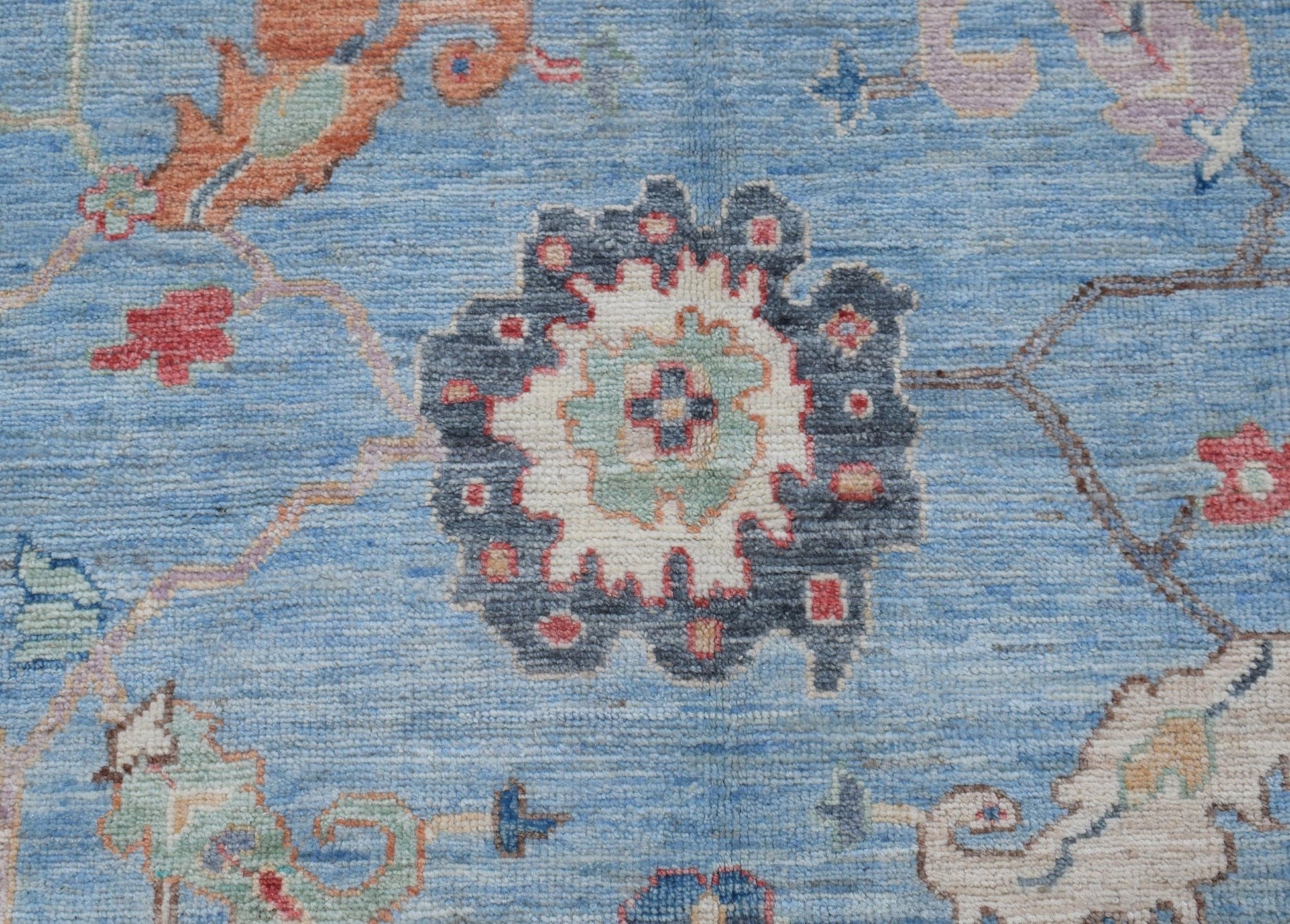 A handwoven transitional Oushak rug featuring a floral pattern in blue, cream, and muted tones.