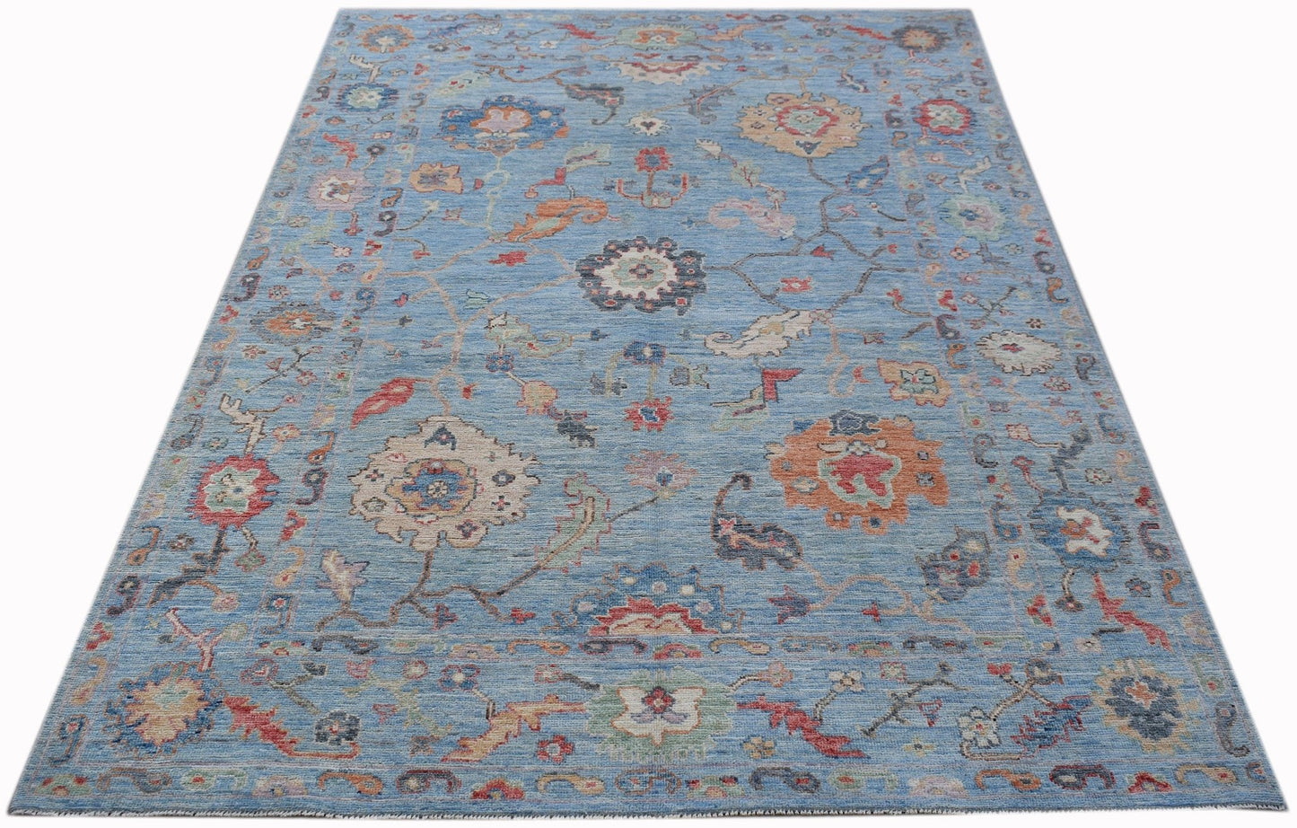 A handwoven transitional Oushak rug featuring a floral pattern in blue and multi-colored tones.