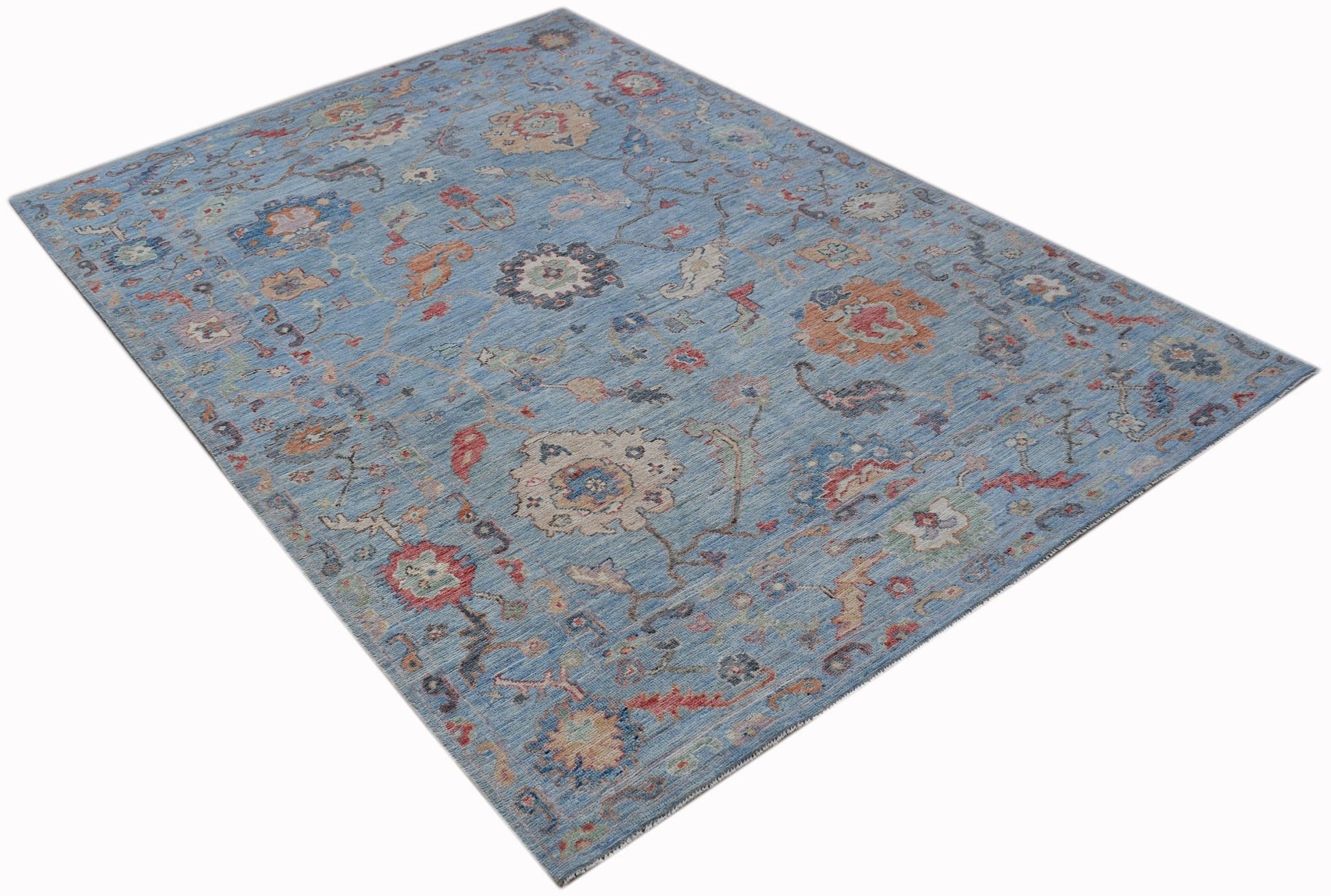A handwoven transitional Oushak rug featuring a floral pattern in blue and multi-colored tones.