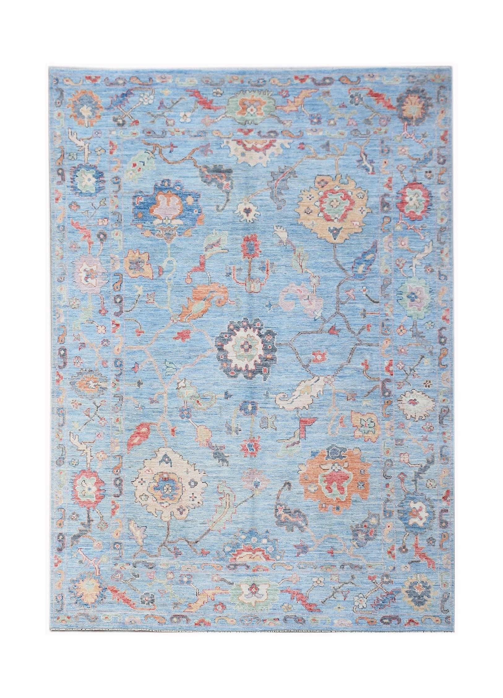 A handwoven transitional Oushak rug featuring a floral pattern in soft colors on a blue background.