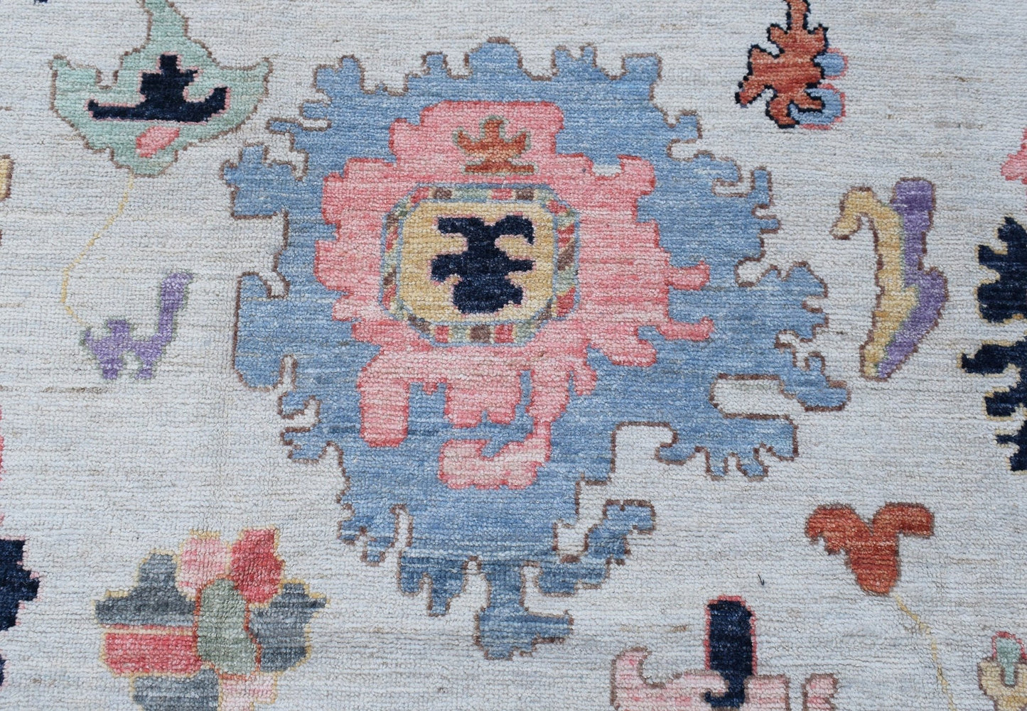 A transitional Oushak rug featuring a central floral motif in pink and blue on a light background.