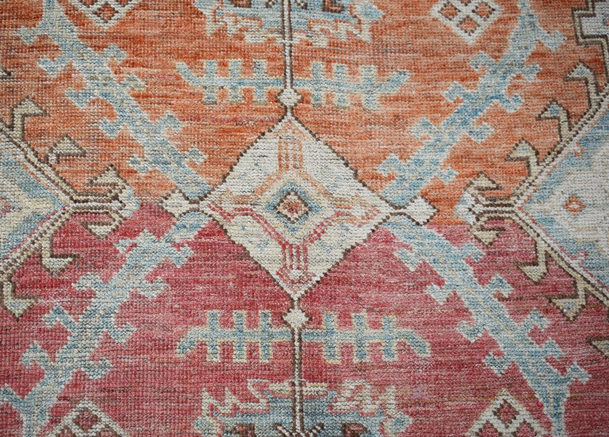 A handwoven transitional Oushak rug featuring a geometric pattern in orange, red, and blue tones.