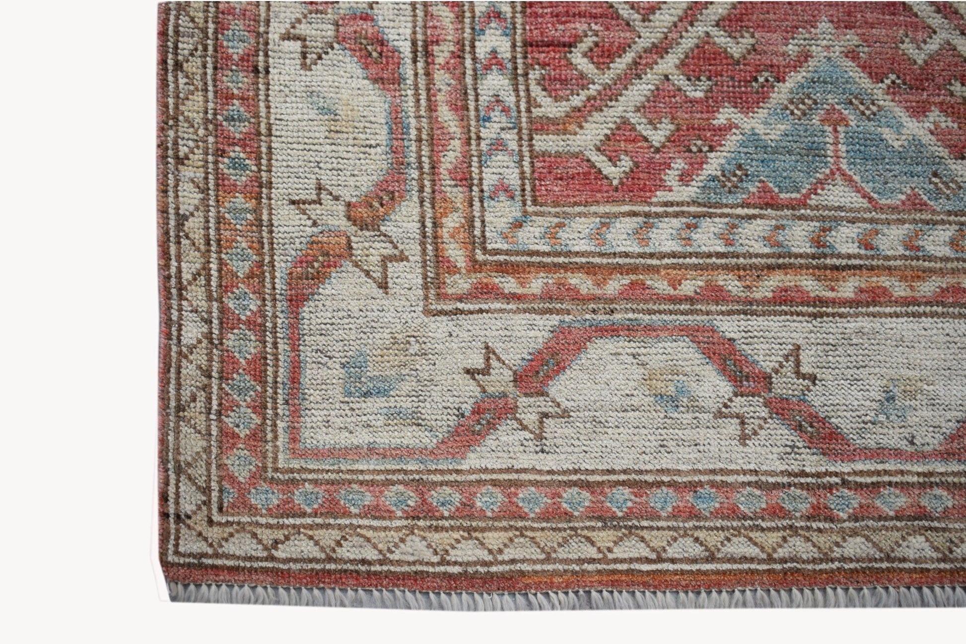 A handwoven wool Oushak rug featuring a traditional floral pattern in red, blue, and cream tones.