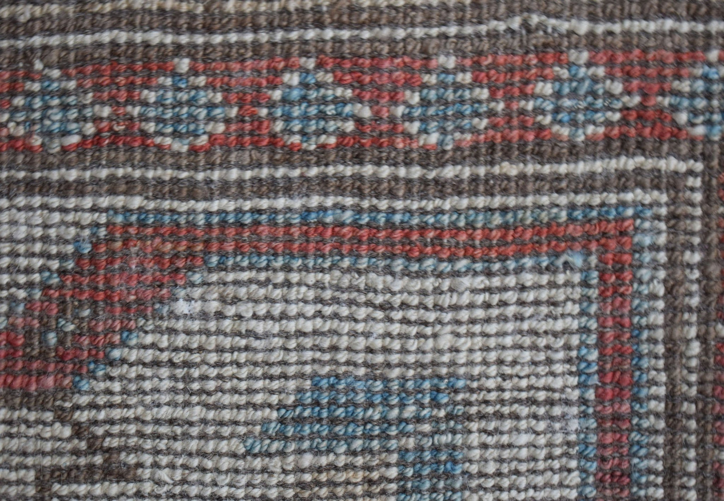 A close-up of a handwoven wool rug featuring a geometric pattern in brown, red, and blue tones.