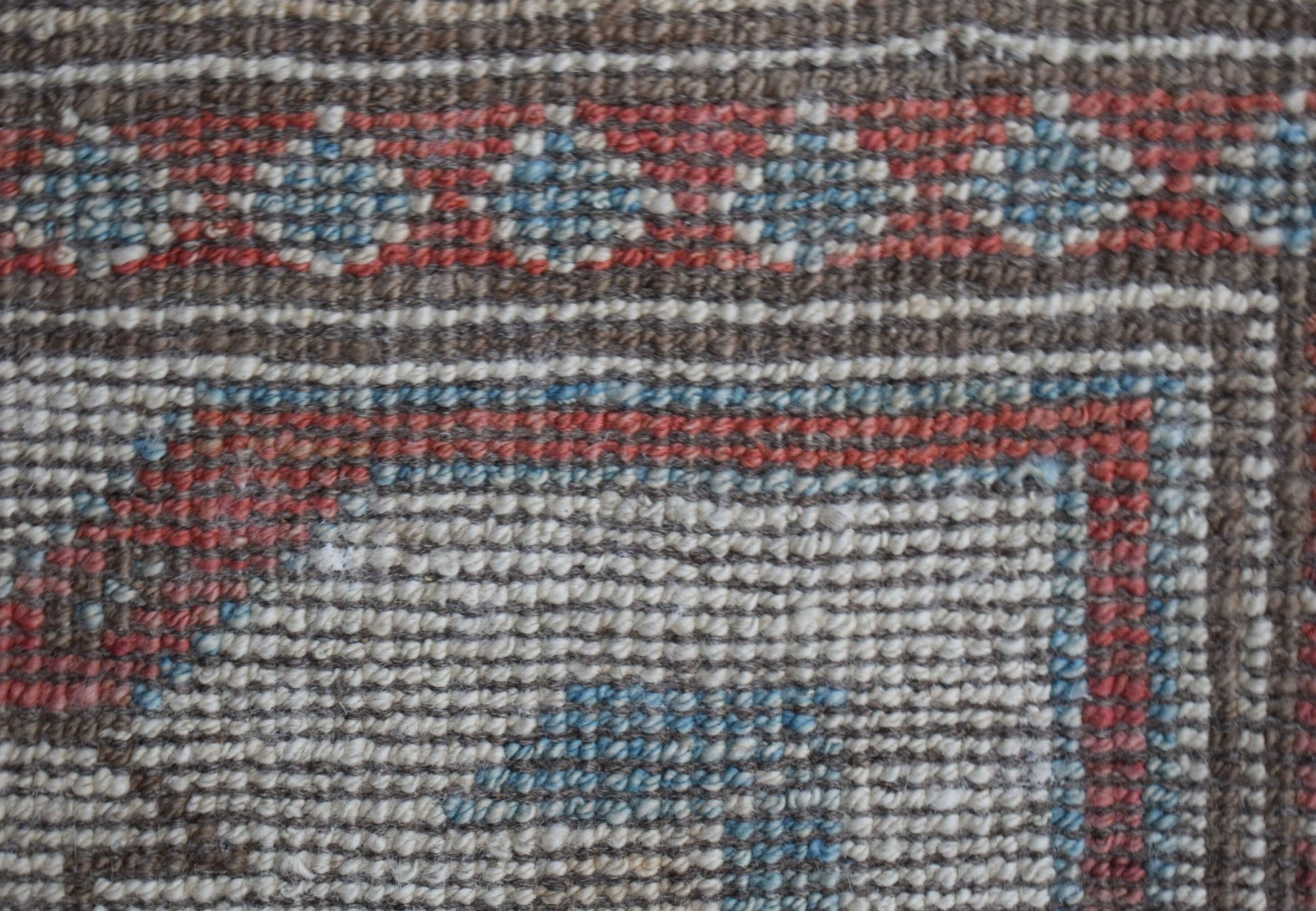 A close-up of a handwoven wool rug featuring a geometric pattern in brown, red, and blue tones.
