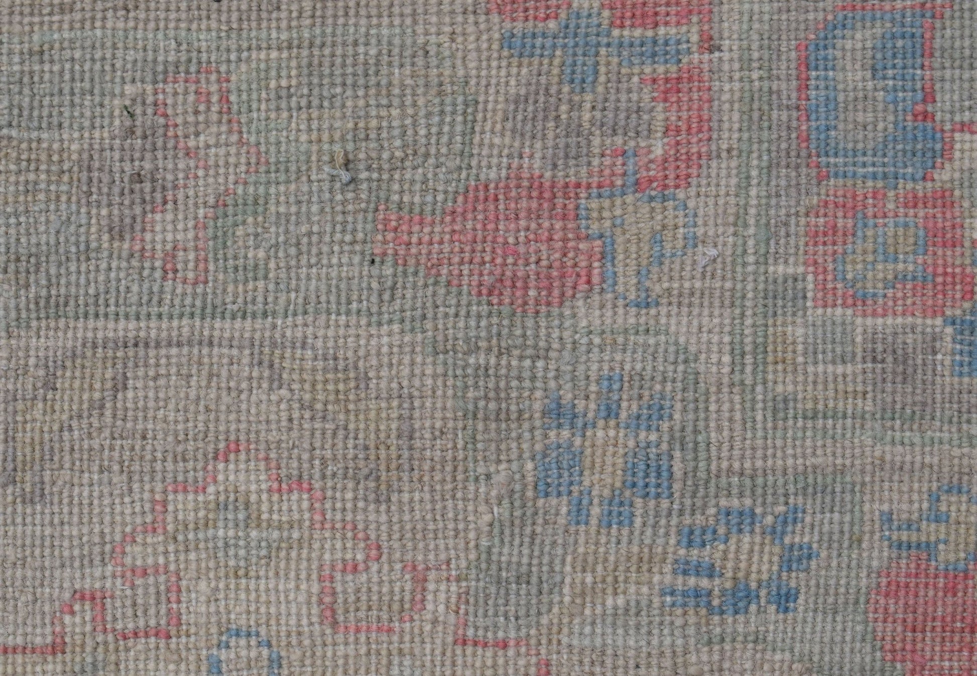 A close-up of a handwoven Oushak rug featuring a floral pattern in soft blue and pink tones.